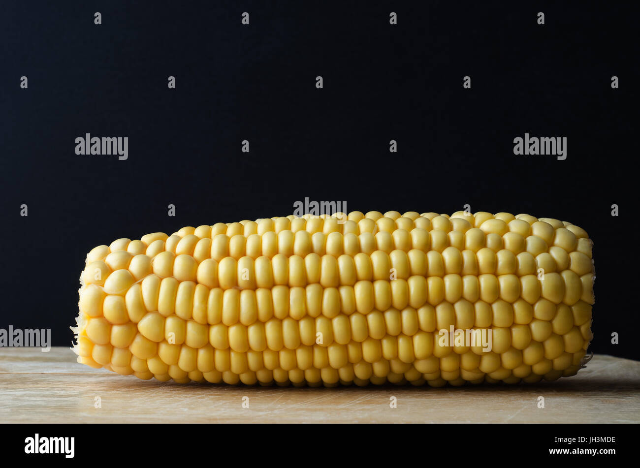 Ein Mais Maiskolben auf hölzernen Schneidebrett Hintergrund schwarze Tafel mit textfreiraum oben. Stockfoto