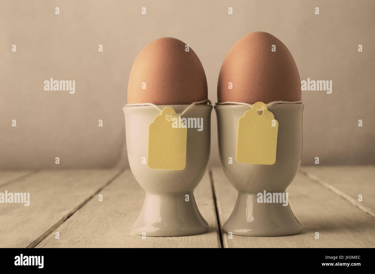 Ein paar braune Eier in Eierbecher mit Preisschild Stil Etiketten auf Zeichenfolge.  Alte weiße geplankte Holztisch.  Farbtöne für retro oder Vintage Auftritt angepasst Stockfoto