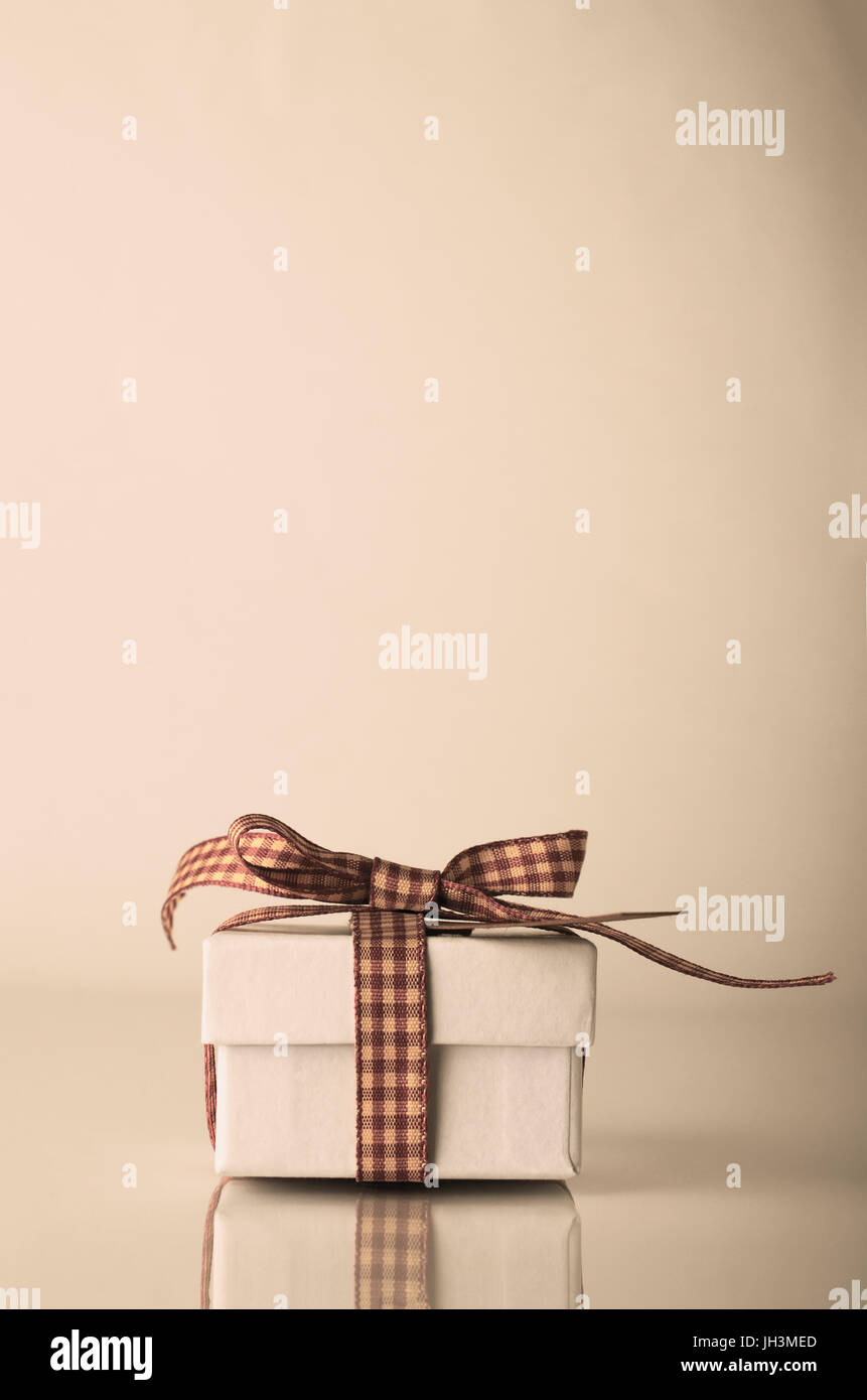 Weiße Weihnachten oder Feier Geschenk-Box mit "Gingham" Band auf reflektierende Oberfläche gebunden.  Farbtöne bereinigt um retro oder Vintage-Effekt.  Raum-Abov kopieren Stockfoto