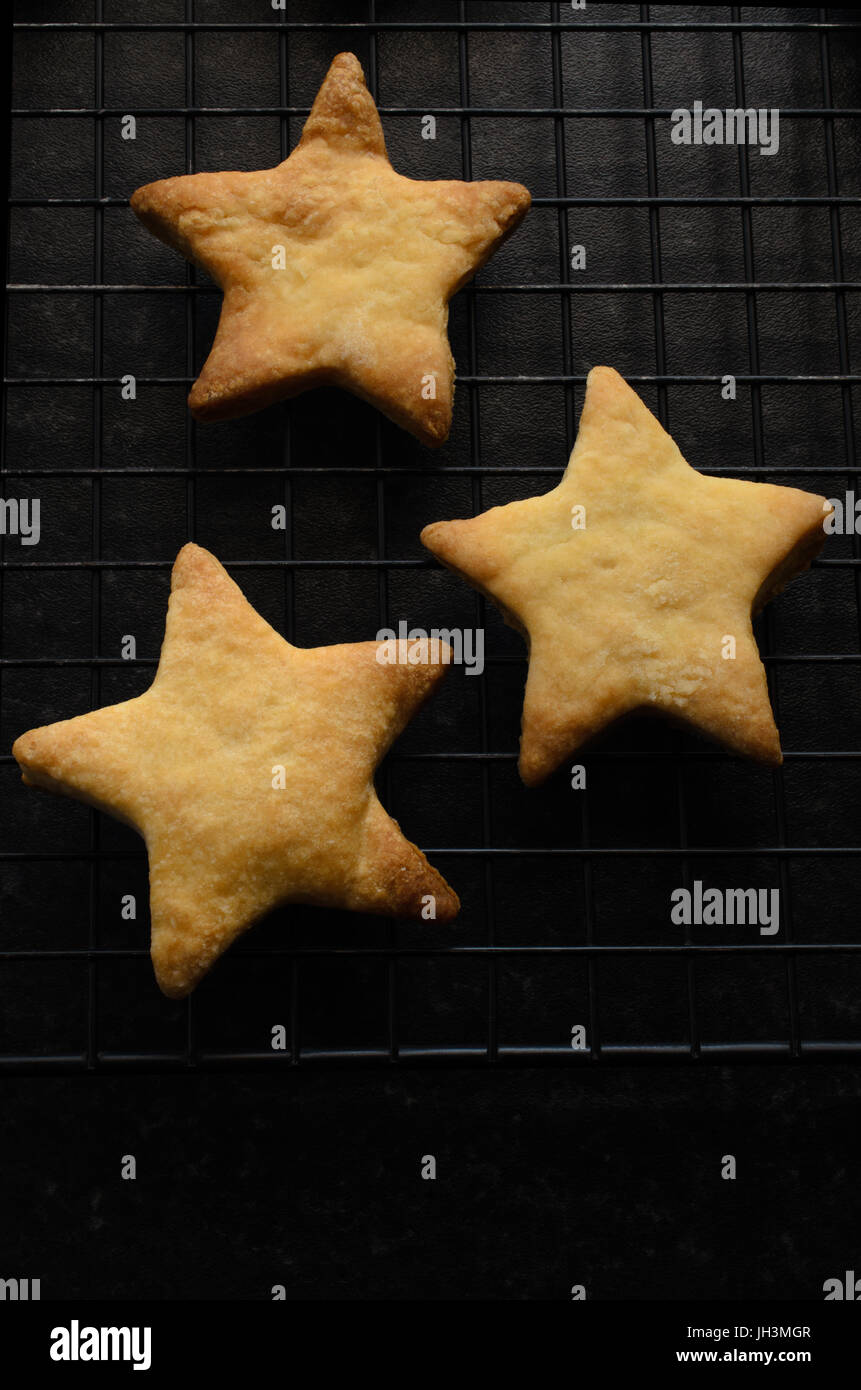 Overhead Schuss von drei sternförmig, gebacken nach Hause Weihnachten Kekse (Cookies) auf einem schwarzen Draht Rack-Kühlung. Stockfoto