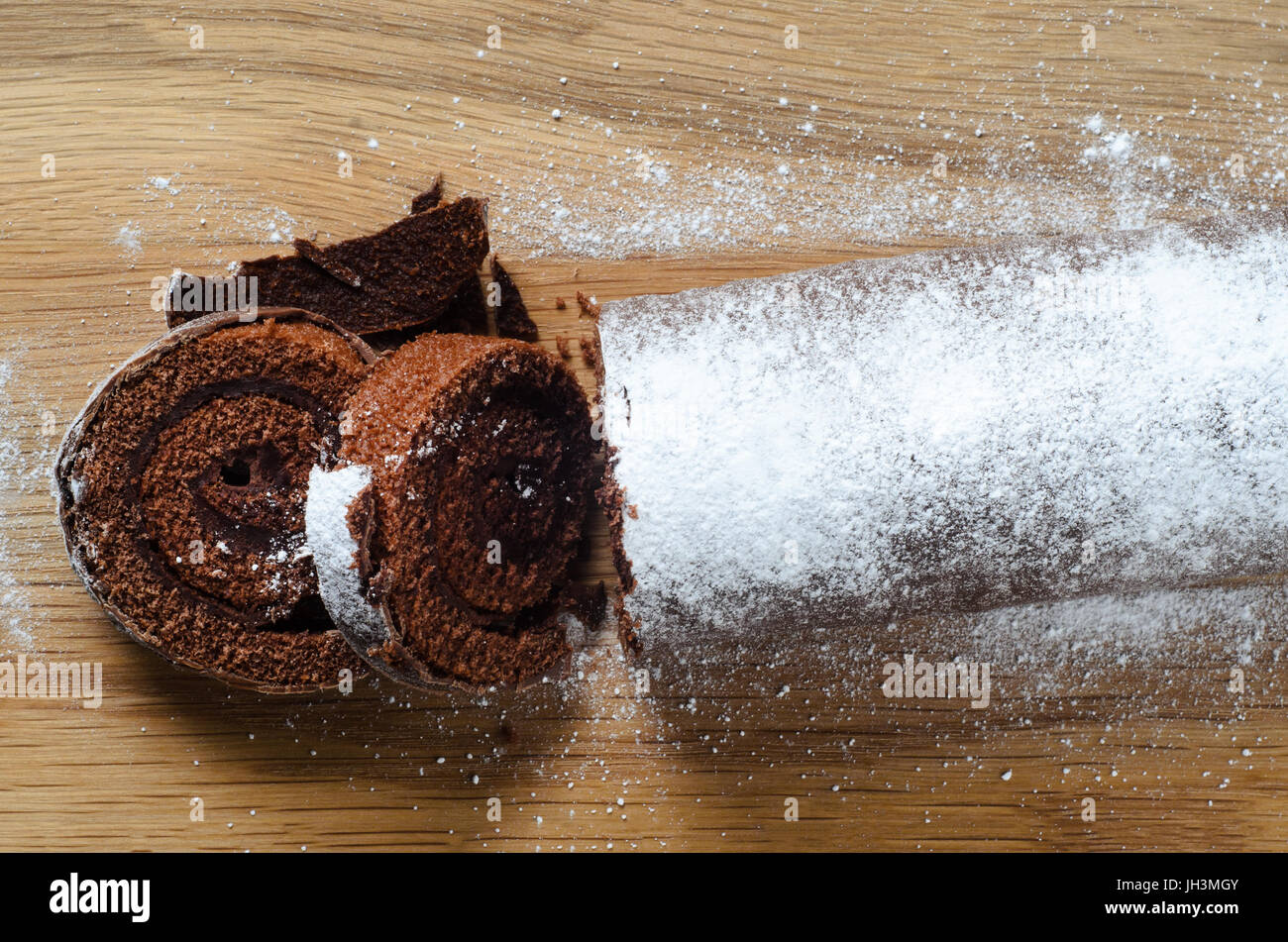 Overhead Schuss ein Weihnachten Yule Log oder Biskuitrolle Schokoladenkuchen, bestreut mit Puderzucker für verschneite Auftritt auf Schneidbrett aus Holz. Stockfoto