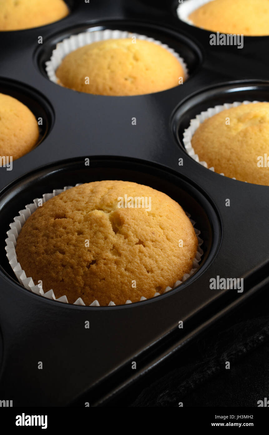 Die Brötchen-Dose gefüllt mit frisch gebackenem golden Vanille Cupcakes in Papier Fällen Kühlung auf schwarzem Schiefer. Stockfoto