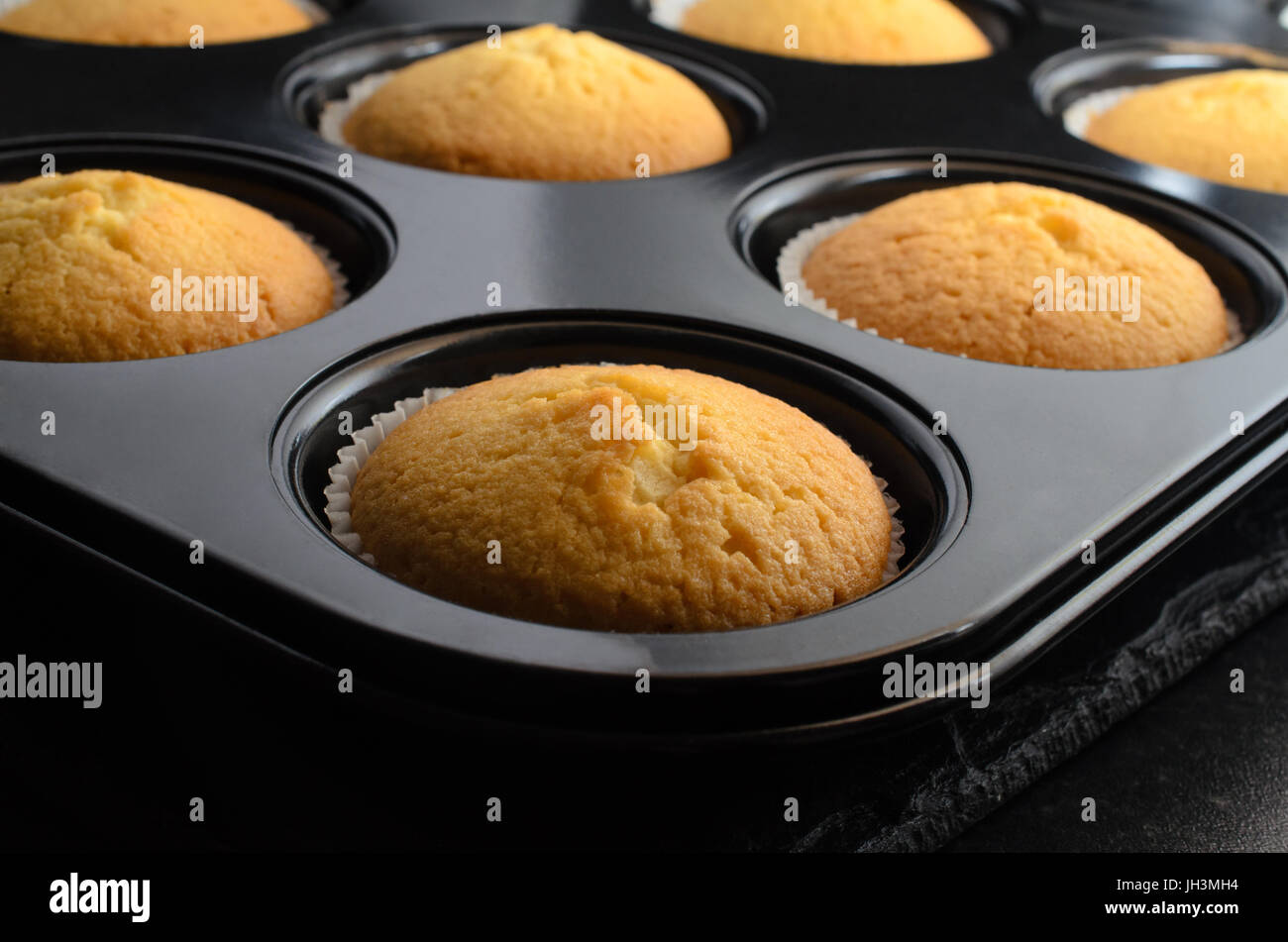 Backen Wohnkonzept mit mehreren Vanille Cupcakes in Papier Fällen innen Brötchen Zinn, Kühlung auf schwarzem Schiefer. Stockfoto