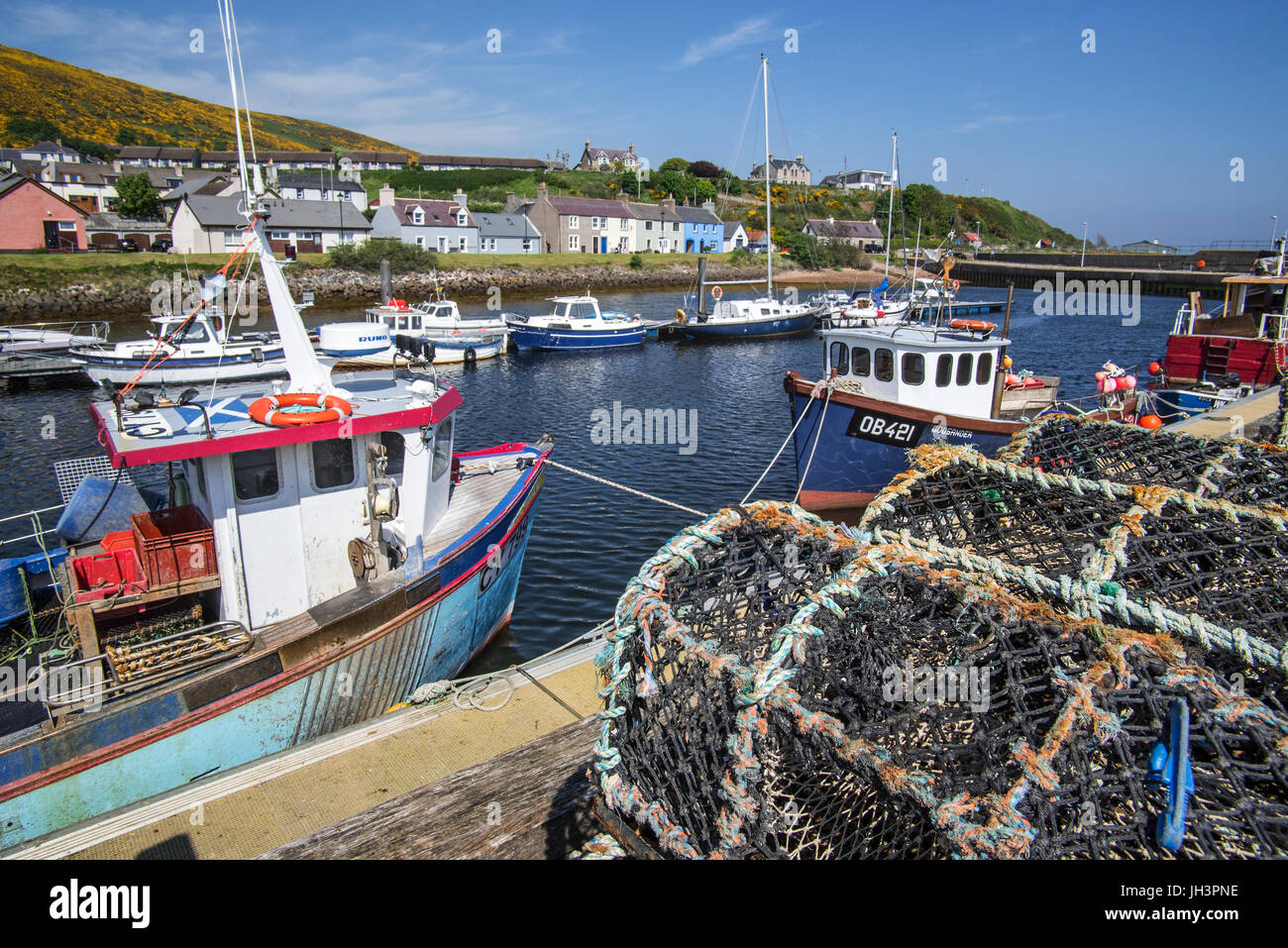 Gestapelte Hummer Gatter / fallen am Kai und Angelboote/Fischerboote im Hafen von Helmsdale, Sutherland, Schottisches Hochland, Schottland Stockfoto