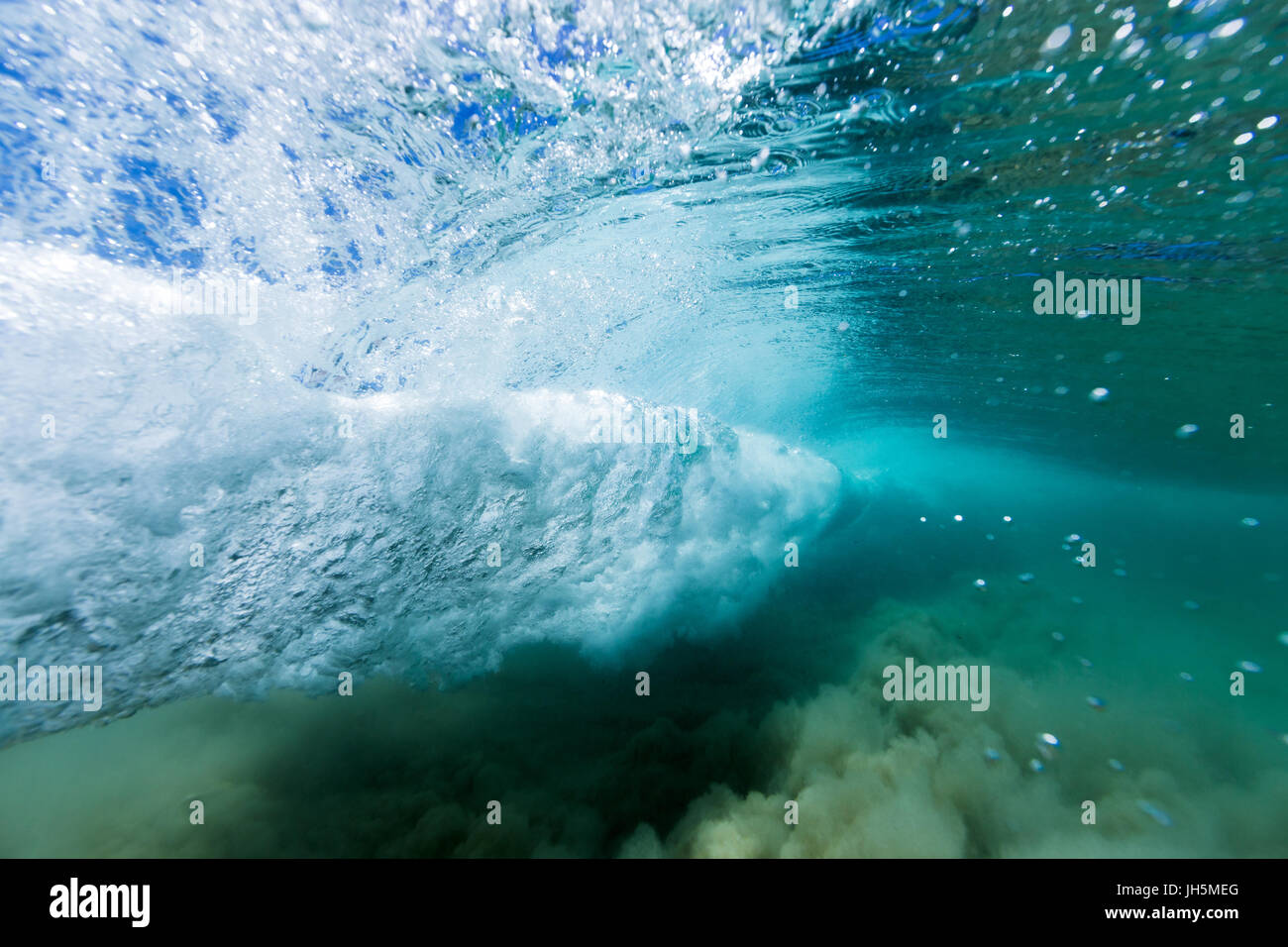 Eine brechende Welle bildet einen Wirbel im kristallklaren Meerwasser in diesem Unterwasser-Bild. Stockfoto