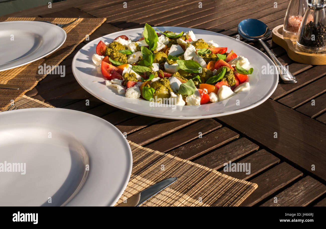 Caprese Salat mit Pesto und kalte gekochte Kartoffeln, auf weissem Geschirr serviert, auf Garten Terrasse Tisch im Sommer Sonnenschein, Schottland, UK Stockfoto