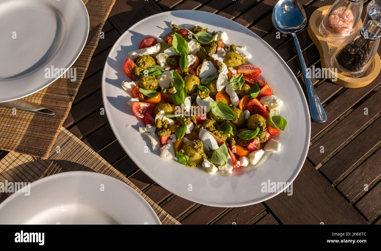 Caprese Salat mit Pesto und kalte gekochte Kartoffeln, auf weissem Geschirr serviert, auf Garten Terrasse Tisch im Sommer Sonnenschein, Schottland, UK Stockfoto