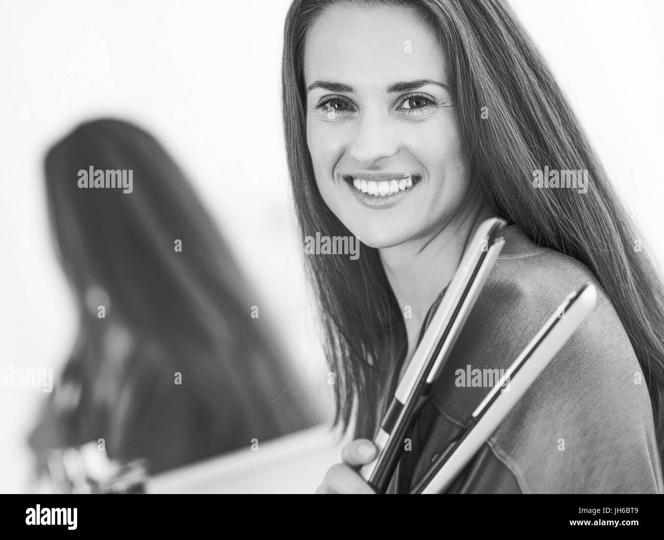 glückliche junge Frau mit Haarglätter im Badezimmer Stockfoto
