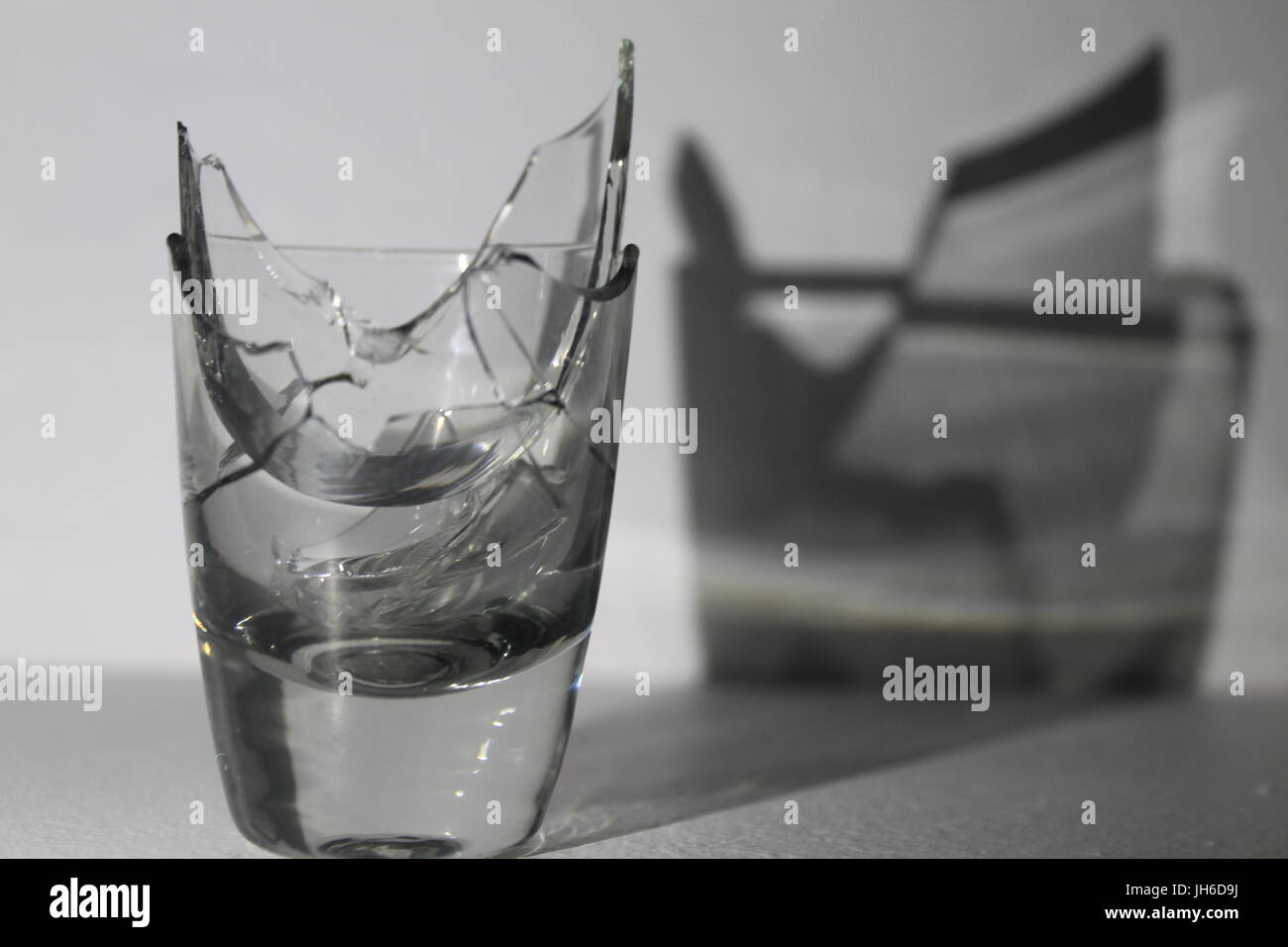 Gebrochene Schnapsglas wirft einen Schatten auf weißem Hintergrund Stockfoto