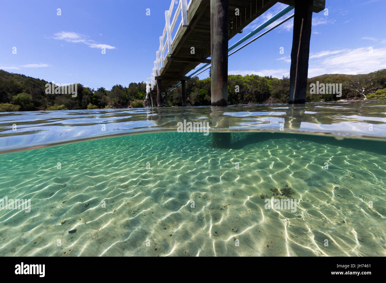 Eine Brücke führt über schöne unberührte Wasser an einem Sommertag in diesem Unterwasser Split-Bild. Stockfoto
