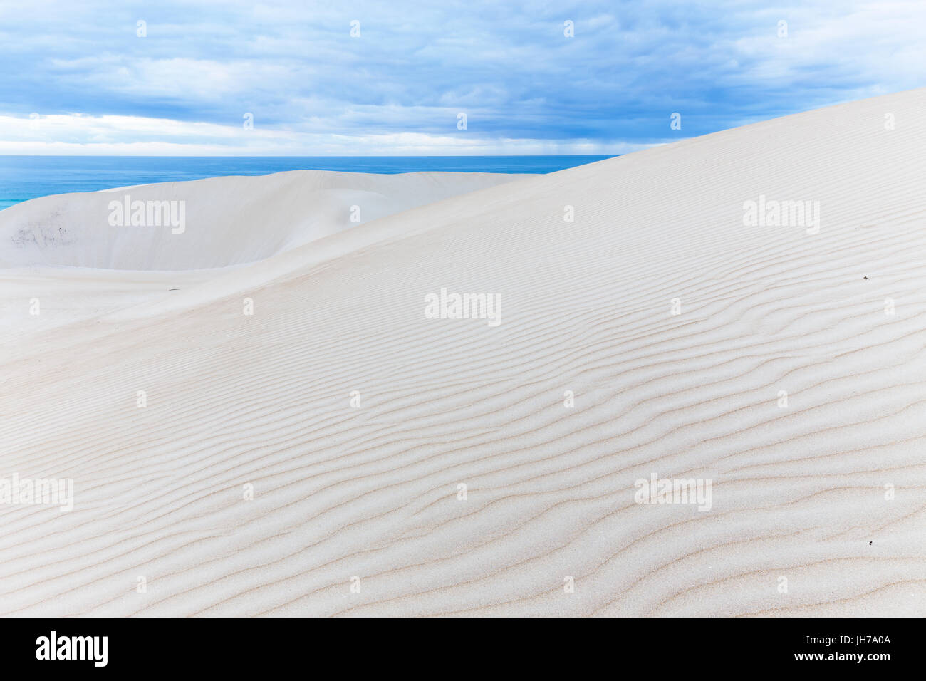 Wunderschöne wellige Dünen treffen den tiefblauen Ozean unter einem Gewitterhimmel in diesem Seelandschaft Hintergrund abstrahieren. Stockfoto