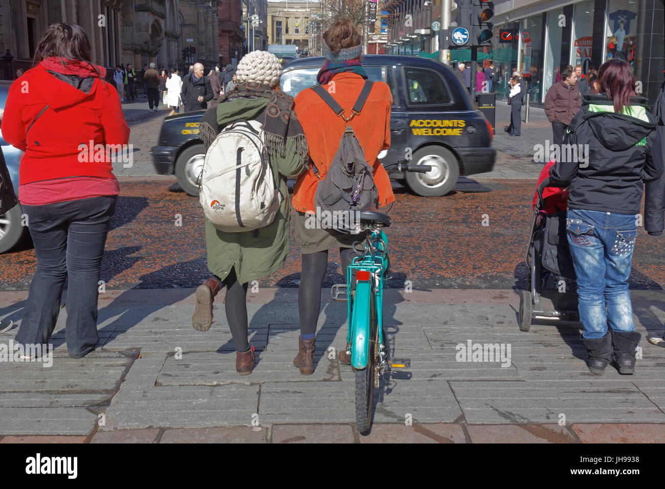 Buchanan Street Fußgänger warten am Bordstein junge Mädchen Radfahrer mit Rucksäcken auf Gehweg Bürgersteig Stockfoto
