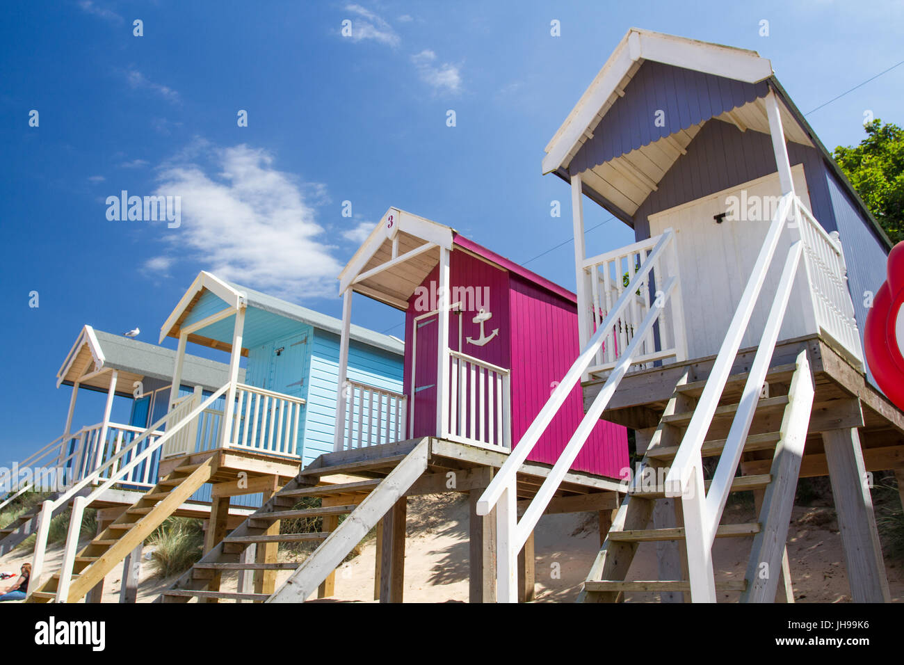 Reihen von bunten Strandhütten auf Stelzen am sonnigen, sandigen Strand von Wells nächsten The Sea in Norfolk, England ist ein beliebtes touristisches Strand in England. Stockfoto