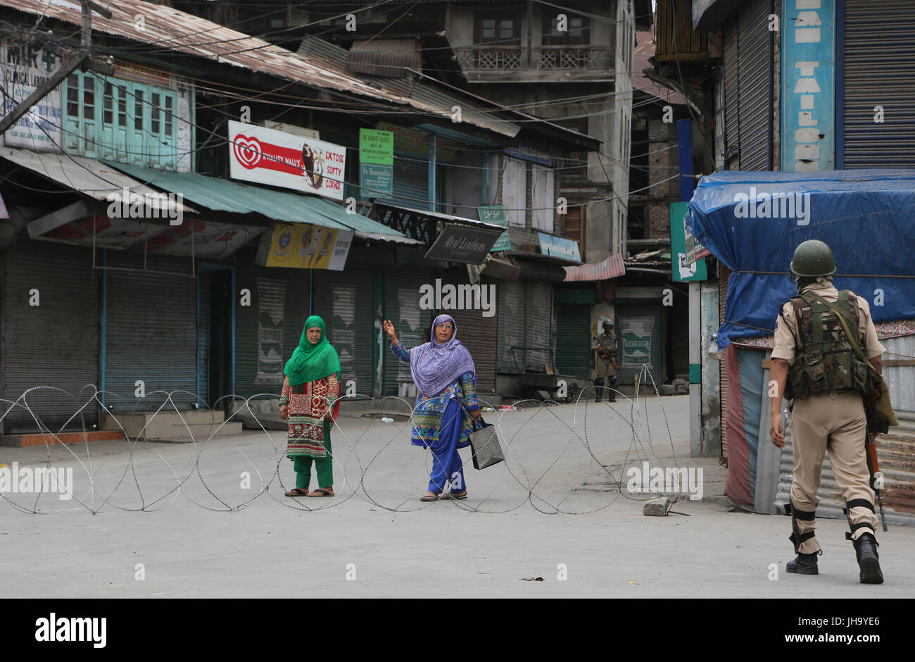 Srinagar, Kaschmir. 13. Juli 2017. Eine indische paramilitärischer Soldat hält Kashmiri Frauen in der Nähe von Stacheldraht Barrikade während der Ausgangssperre-ähnliche Einschränkungen in Srinagar, Sommer Hauptstadt OfKashmir, 13. Juli 2017. Bildnachweis: Javed Dar/Xinhua/Alamy Live-Nachrichten Stockfoto