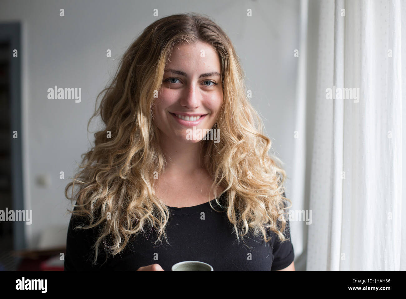 Jung, blond, schöne kaukasischen Frau bei einem heißen Getränk in der Nähe der Fenster im natürlichen Morgenlicht. Drinnen im Sommer auf einer Canon 5D aufgenommen Stockfoto