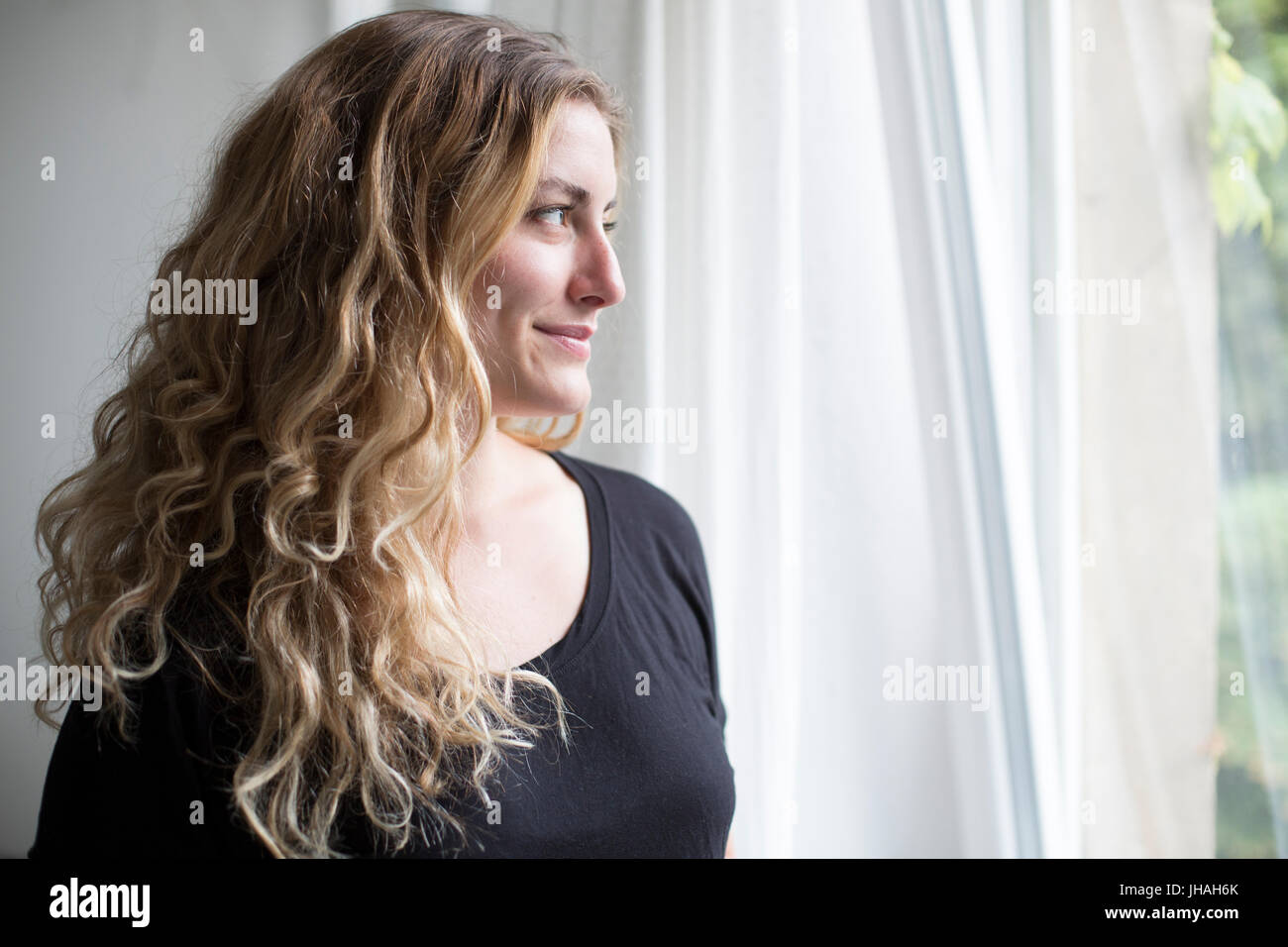 Jung, blond, schöne kaukasischen Frau bei einem heißen Getränk in der Nähe der Fenster im natürlichen Morgenlicht. Drinnen im Sommer auf einer Canon 5D aufgenommen Stockfoto