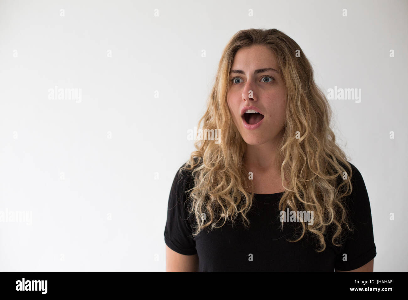 Jung, blond, schön, kaukasischen Milennial Frau zum Ausdruck bringen Aufregung und Glück während winken vor einem weißen Hintergrund. Einladend, begrüßen. Stockfoto