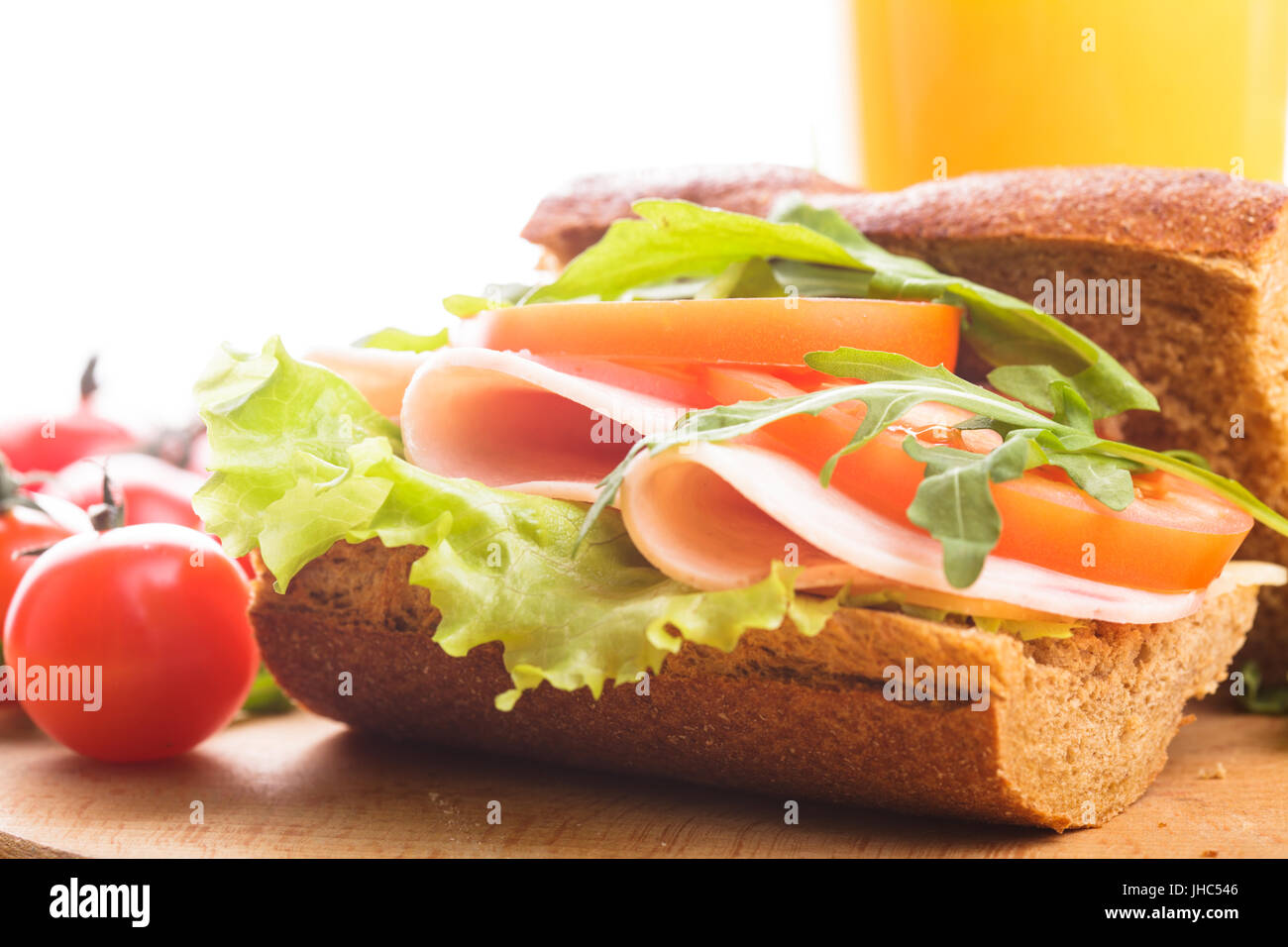 Vollkorn-Sandwich mit Schinken, Tomaten, Lattuce und Rucola mit Glas Orangensaft. Frühstück Stockfoto