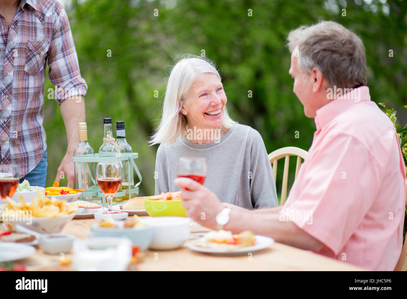 Älteres paar unterhalten zusammen auf einer Gartenparty. Sie trinken Wein und Grill Essen. Stockfoto