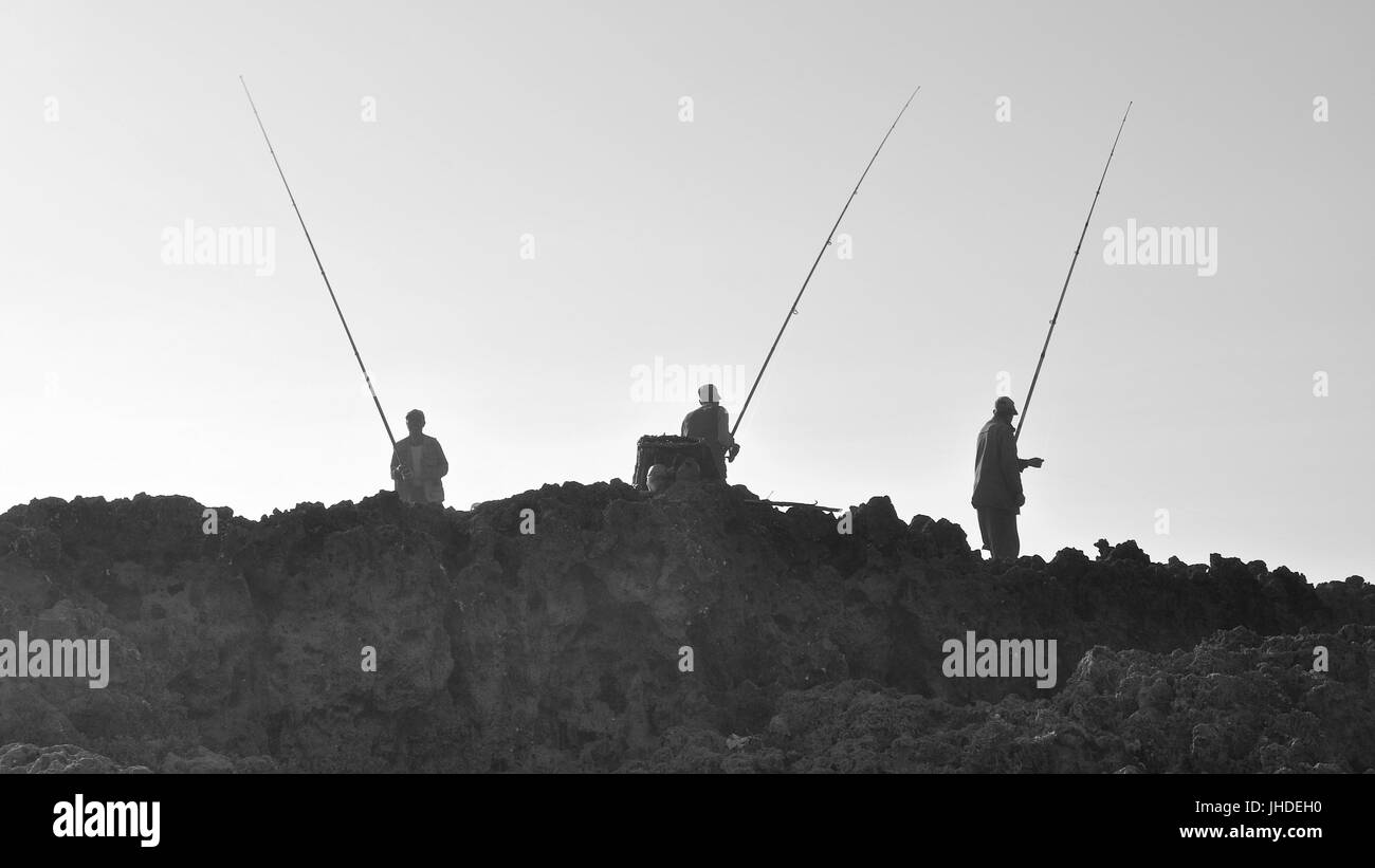 Beleuchtete Silhouetten von lokalen angler Fischer über schroffe Felsen in Oualidia Atlantikküste (El Jadida, Casablanca-Settat, Marokko) Stockfoto