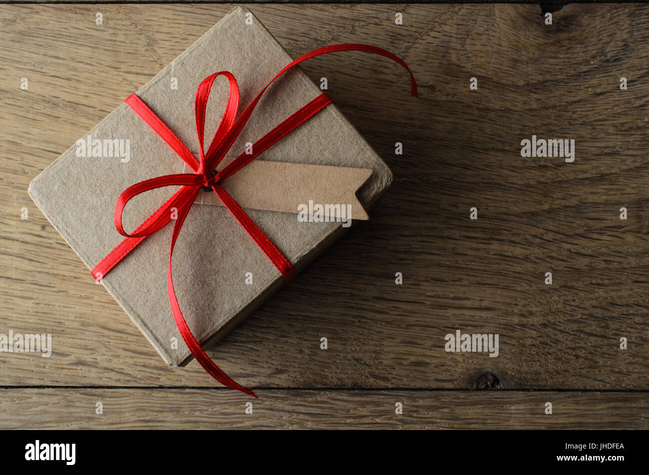 Overhead Schuss eine schlichte braune Geschenkbox mit Weihnachten Red Ribbon und eine leere Beschriftung für textfreiraum Set auf alte Eiche Holz Beplankung. Stockfoto