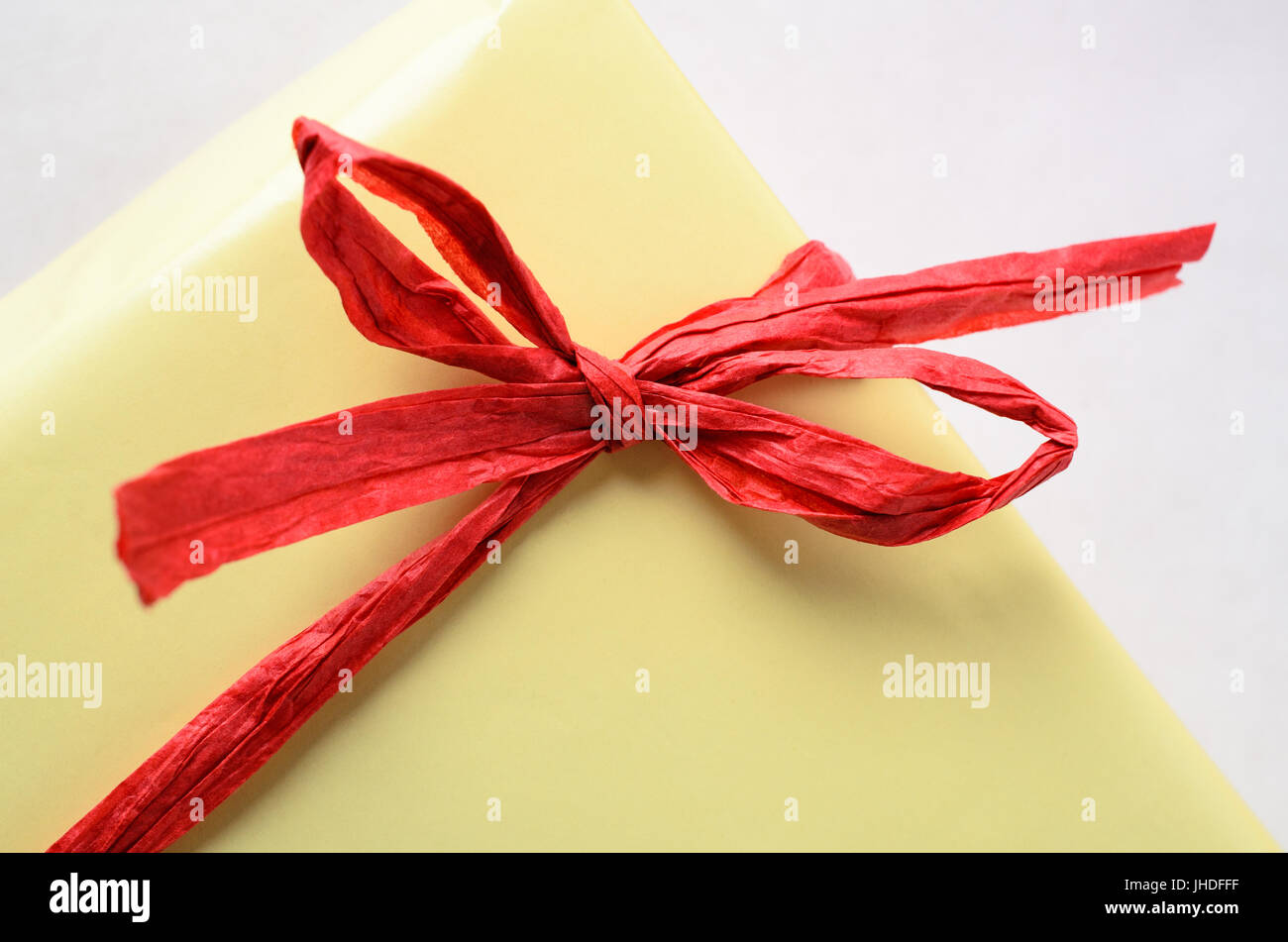 Nahaufnahme von einem gebundenen roter Bast Bogen um eine gelbe Geschenkpackung verpackt. Stockfoto