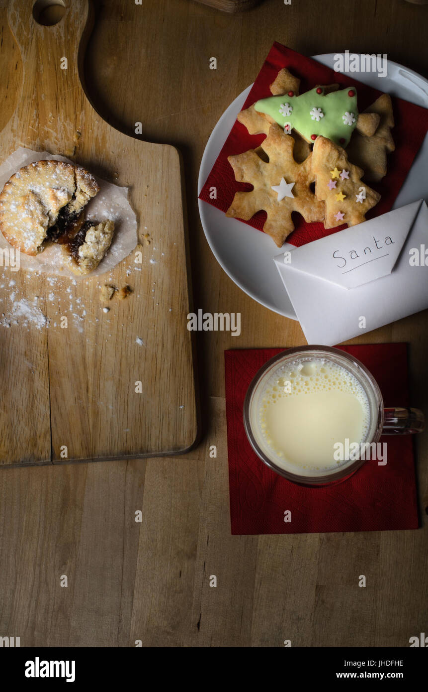 Overhead Schuss auf Holztisch Kekse (Cookies), Milch und Mince Pies, ausgelassen am Heiligabend für Santa, mit Liste in Umschlag. Stockfoto