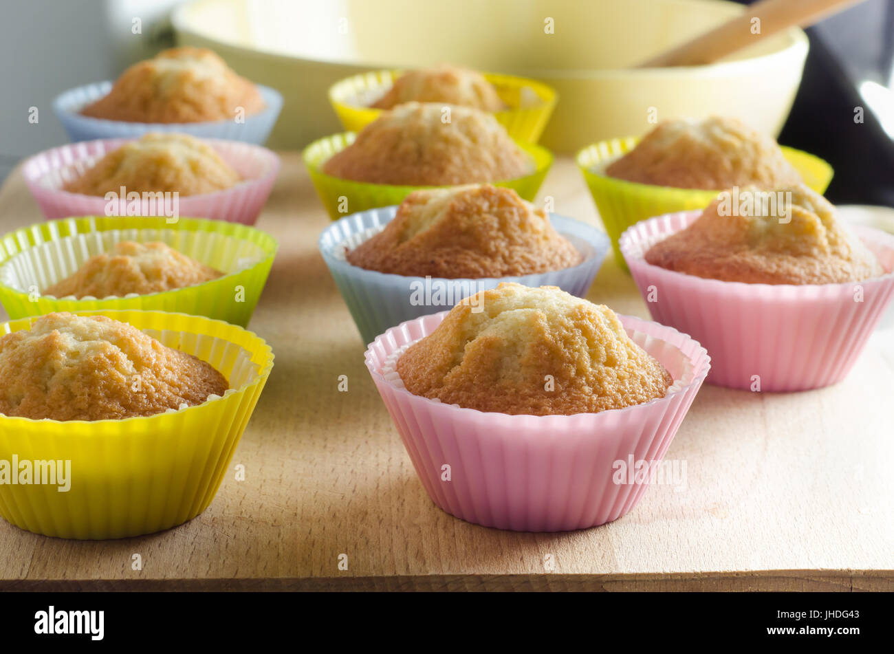 Zu Hause Backen Küche-Szene. Zeilen der frisch gebackene Muffins auf hölzernen Schneidebrett mit Misch-Schüssel und Löffel im Hintergrund. Stockfoto
