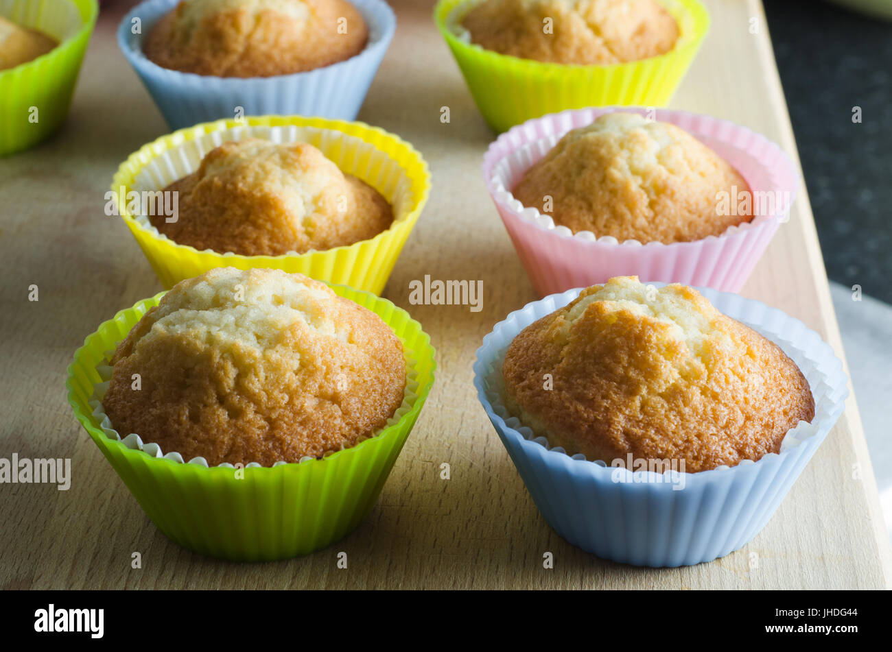 Zeilen der frisch gebackene Muffins auf Schneidbrett aus Holz in hellen, bunten Silikon Fällen. Stockfoto