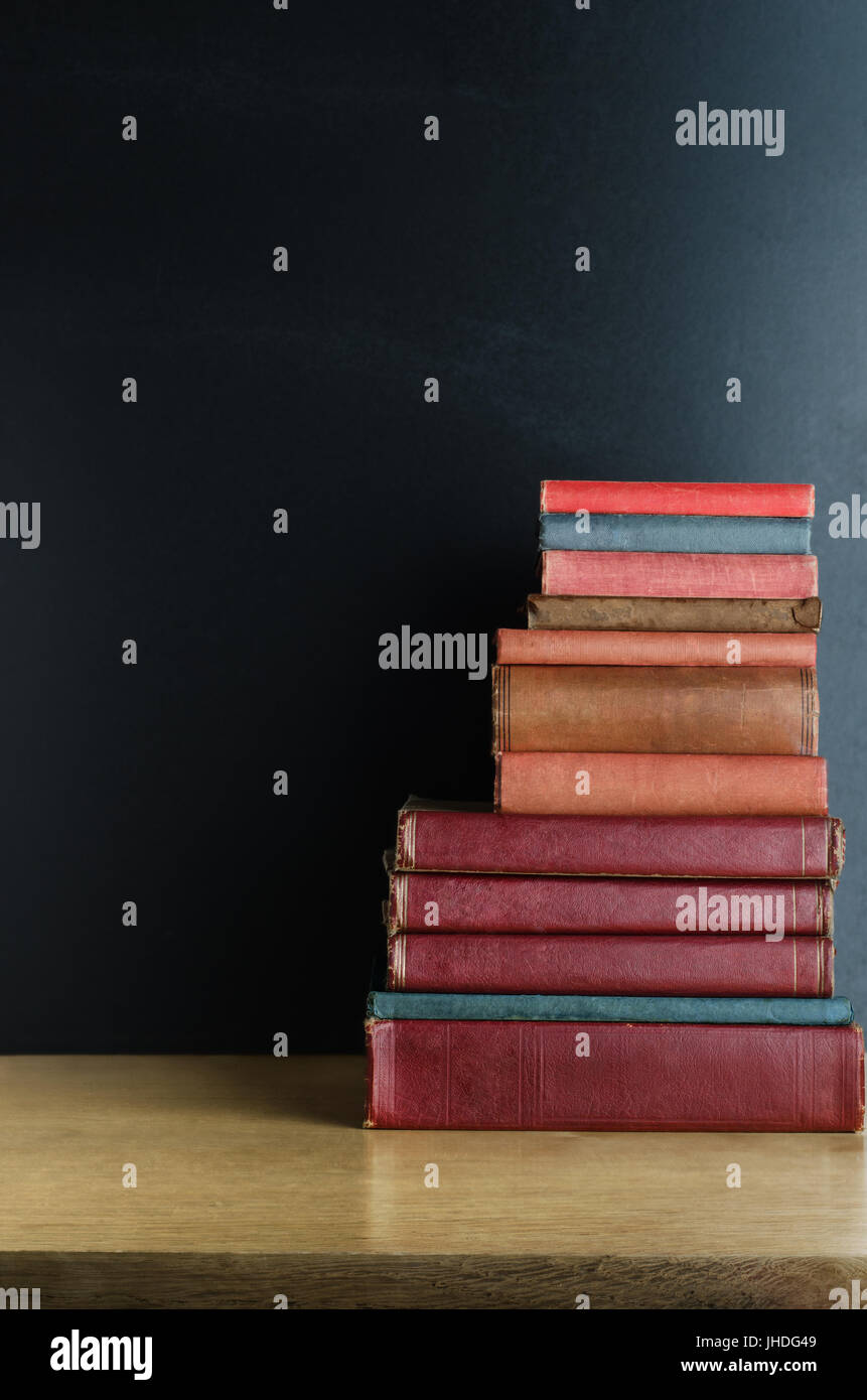 Ein Haufen Alter, verwendet Textbücher gestapelt in einem Haufen auf einem hölzernen Schreibtisch vor einer schwarzen Tafel.  Kopieren Sie Raum nach links und oben. Stockfoto