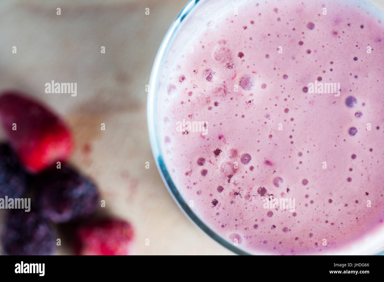 Overhead Nahaufnahme einer schaumigen rosa Smoothie aus Sommerfrüchten und Sojamilch hergestellt. Stehend auf Holz mit gefrorenen Beeren in soft-Fokus nach links Stockfoto