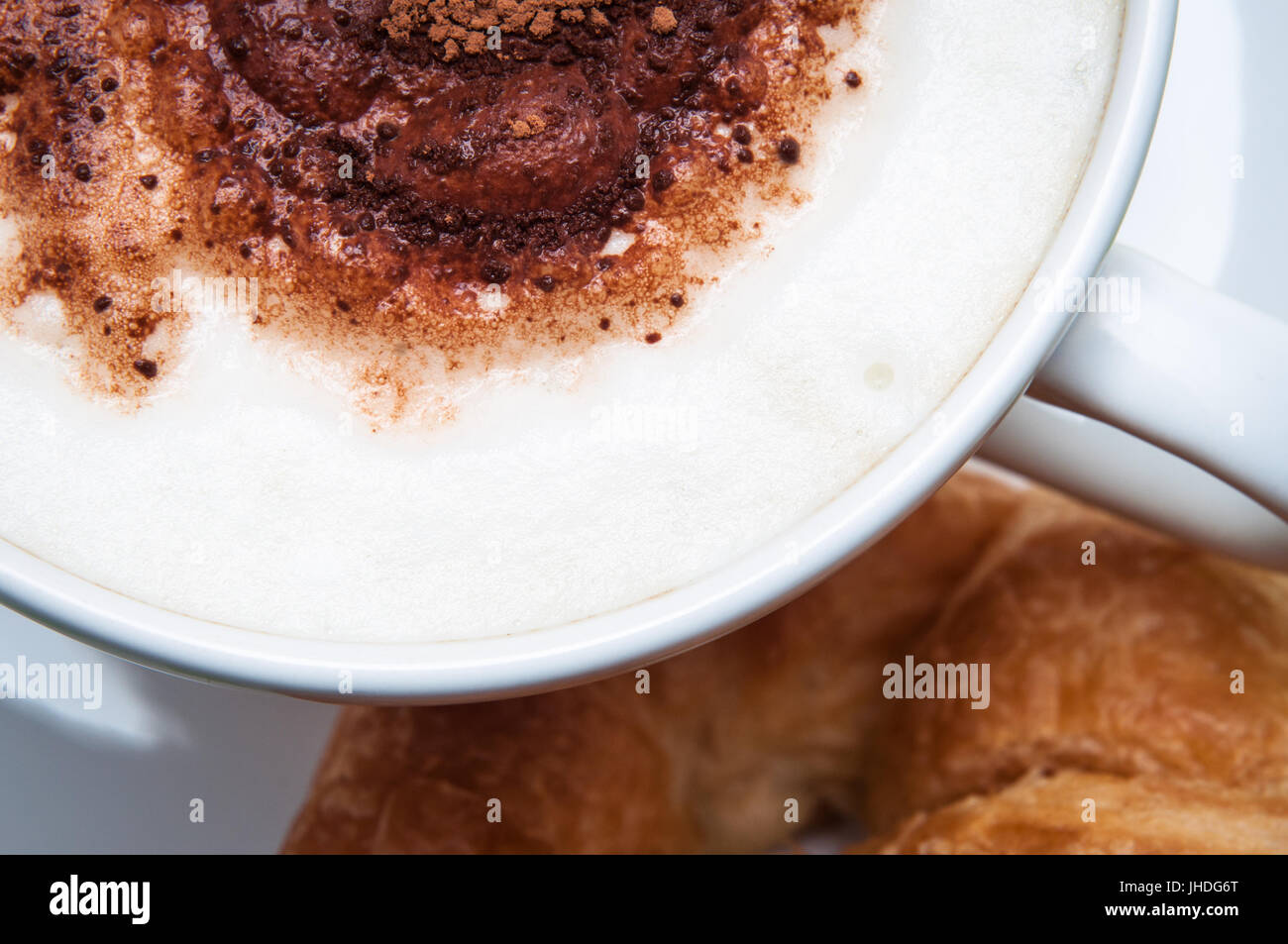 Overhead Schuss einen Latte oder Cappuccino Stil Kaffee mit Kakao Streusel und ein Croissant. Stockfoto