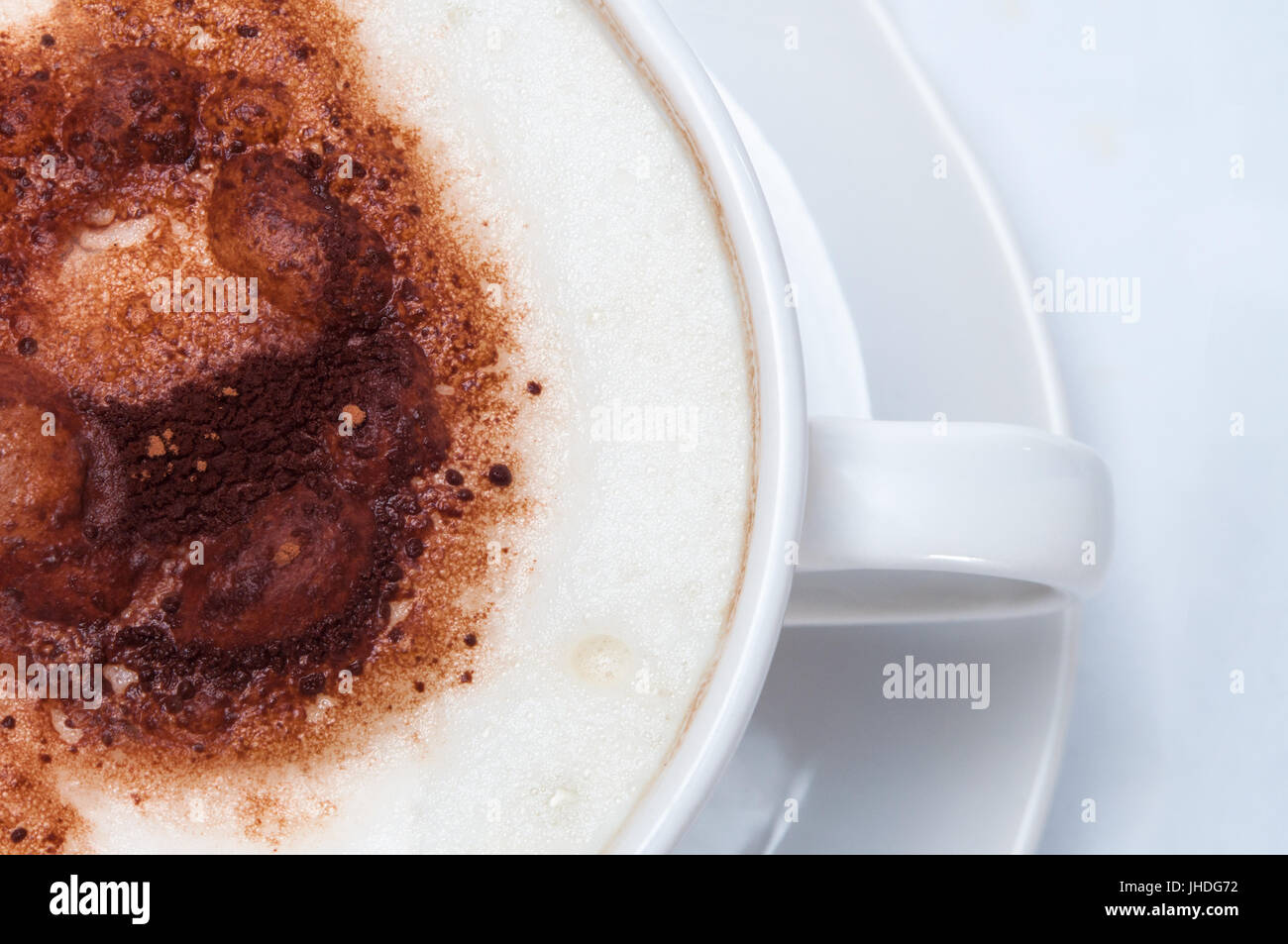 Overhead Schuss Milch Schaum und Kakao Topping aus einem in weiße Tasse mit Untertasse Kaffee Latte oder Cappuccino Stil. Stockfoto