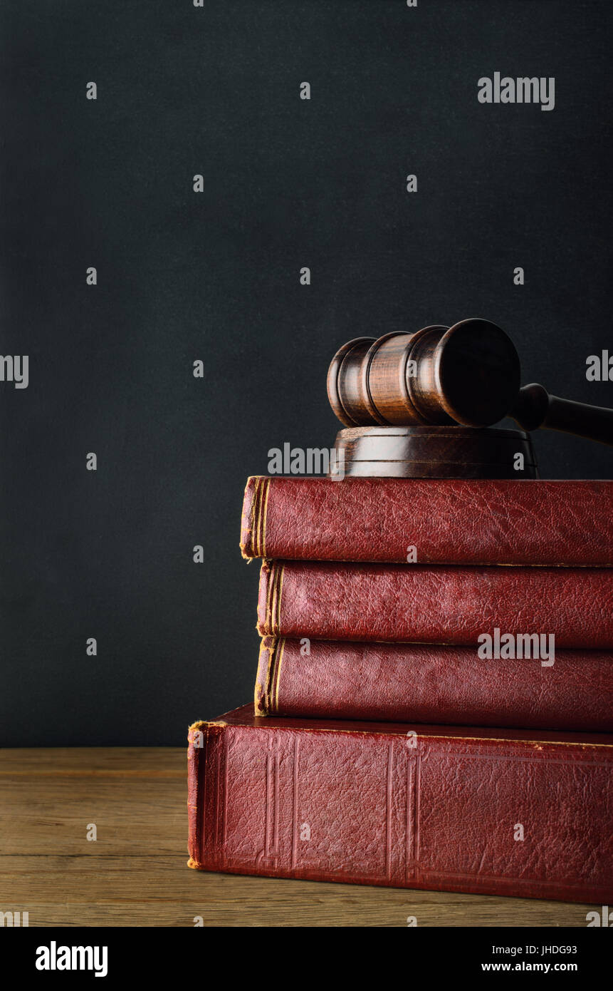 Dunkles Holz Hammer auf einen Stapel gebrauchte Alter Bücher mit leeren Buchrücken, auf Eiche Schreibtisch mit schwarzen Tafel Hintergrund. Stockfoto