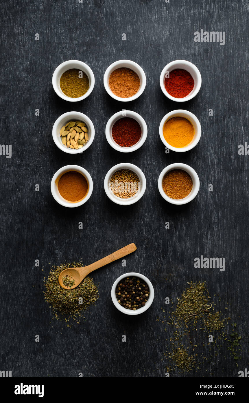 Overhead, Flatlay Schuss von einer Vielzahl von Gewürzen in weißen Schalen mit vereinzelten Kräutern und Holzlöffel auf staubigen Tafel. Stockfoto