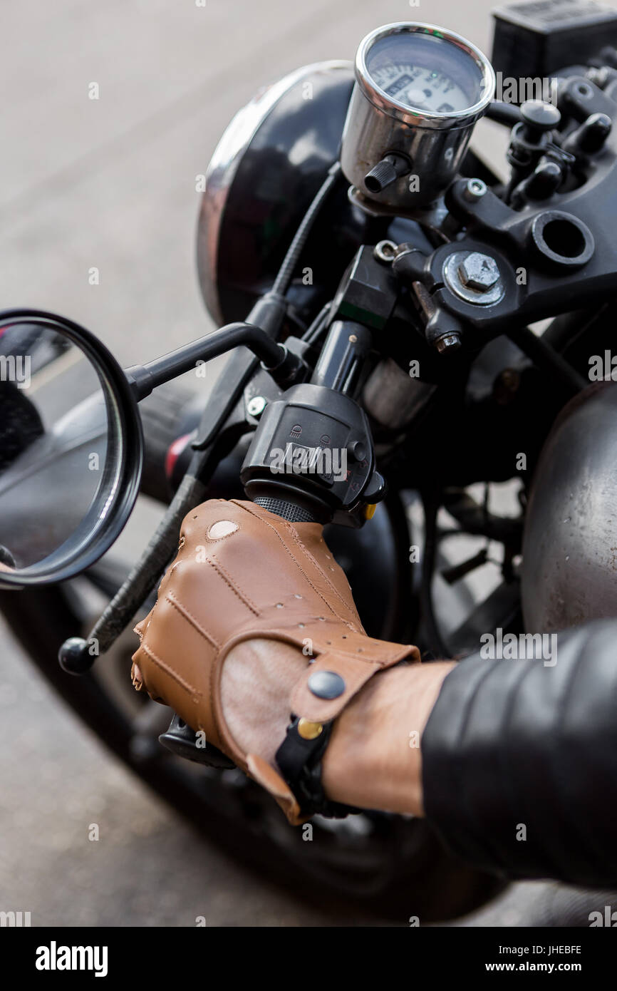 Nahaufnahme einer Hipster Biker Kerl Hand in Leder Handschuh Halt Gashebel des klassischen Stil Café Racer Motorrad. Fahrrad benutzerdefinierte gemacht in Oldtimer garage Stockfoto