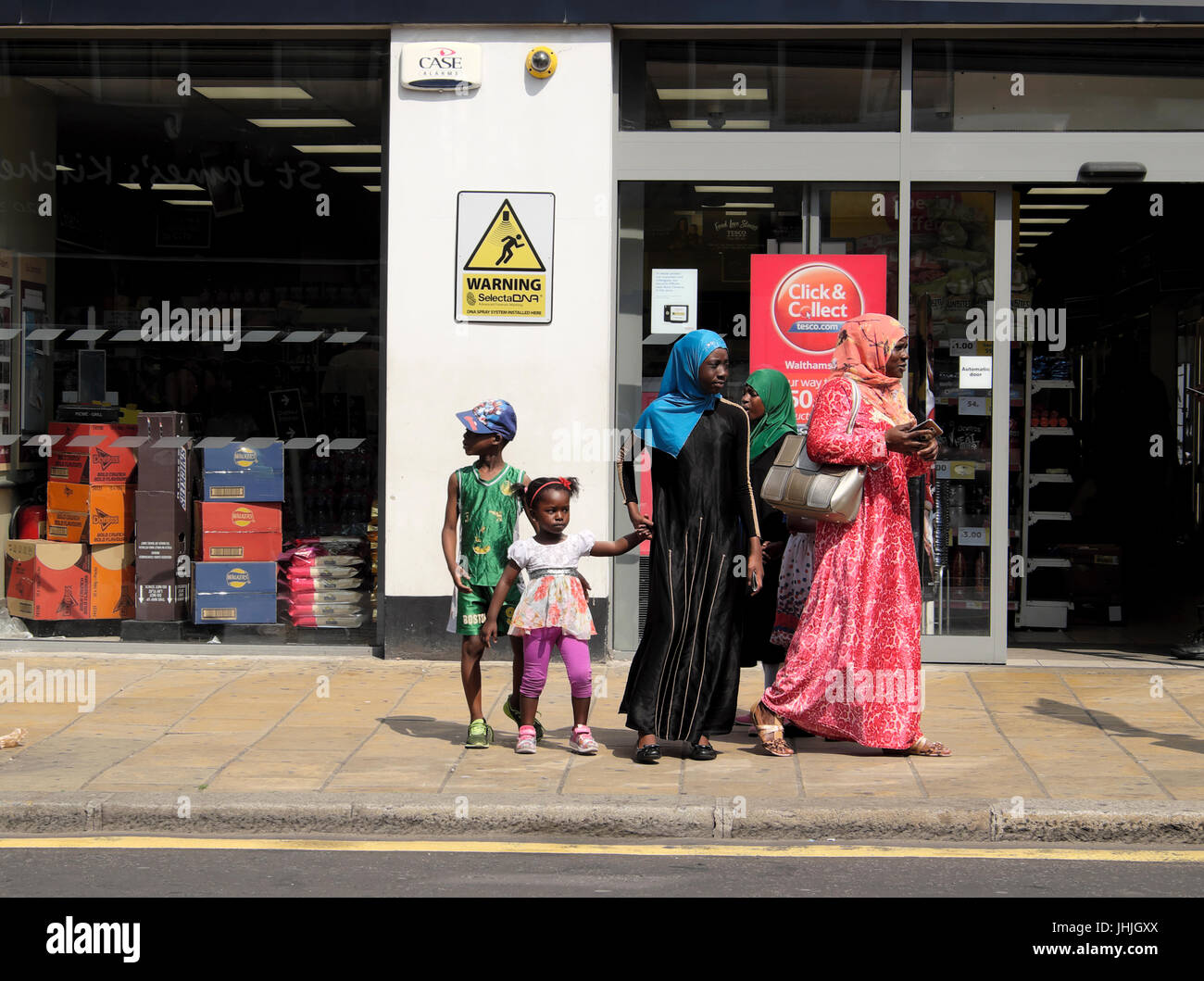 Afrikanische muslimische Familie Mutter Töchter, Kinder warten auf einen Bus vor einem Geschäft in London UK KATHY DEWITT Stockfoto