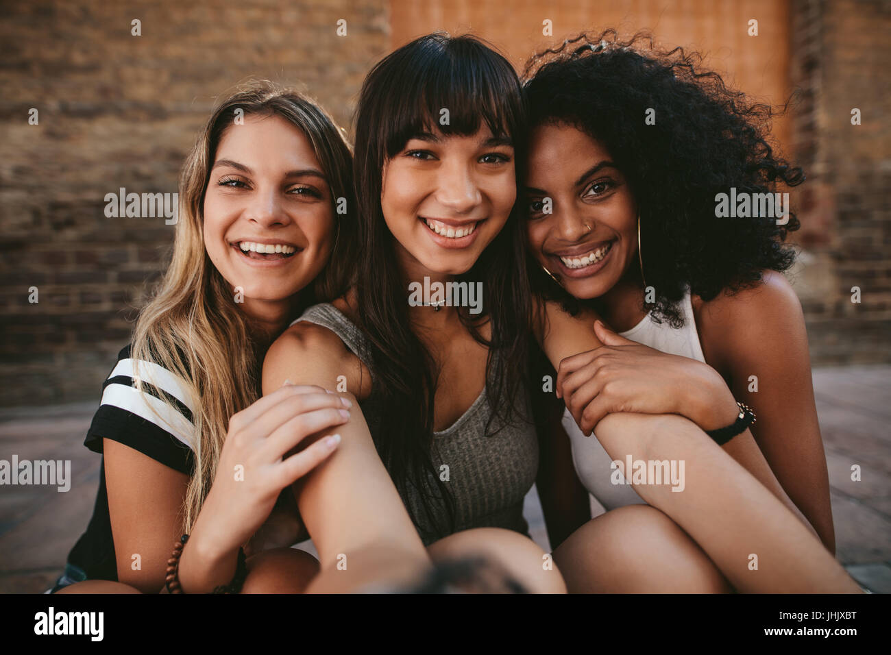 Drei schönen lächelnden Freundinnen nehmen Selfie mit Handy. Multi ethnischen Gruppe von Frauen die Stadtstraße im Freien sitzen und nehmen selbst p Stockfoto