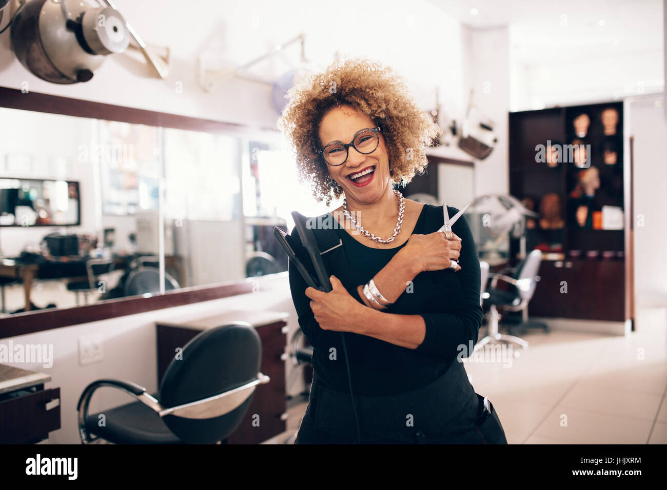 Lächelnde Frauen Friseur hält einen Haarglätter und Schere. Beauty-Salon mit professionellen Friseur gut ausgestattet. Stockfoto