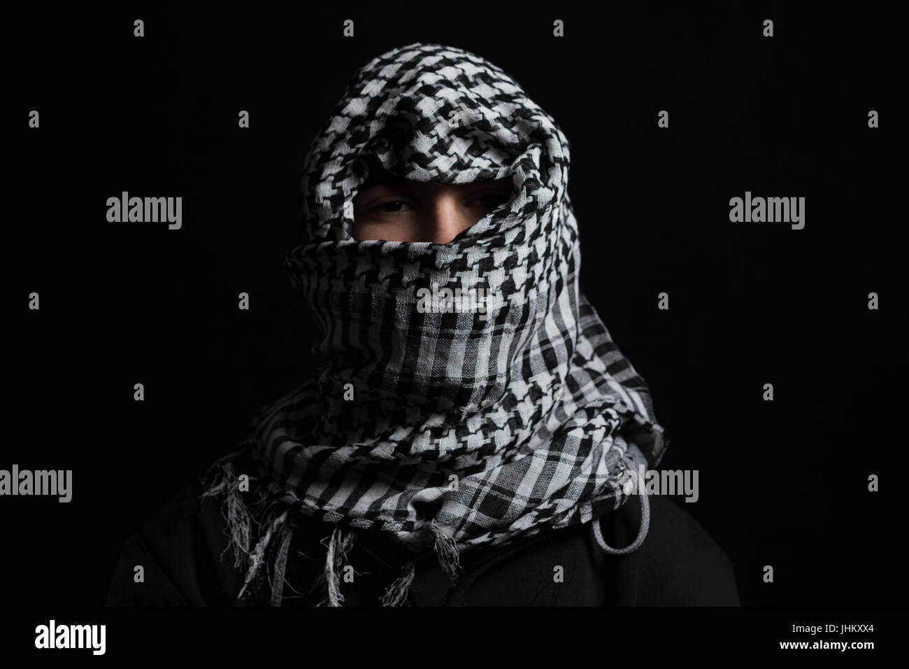 versteckte Mann mit Palästinensertuch über Kopf vor schwarzem Hintergrund isoliert Stockfoto