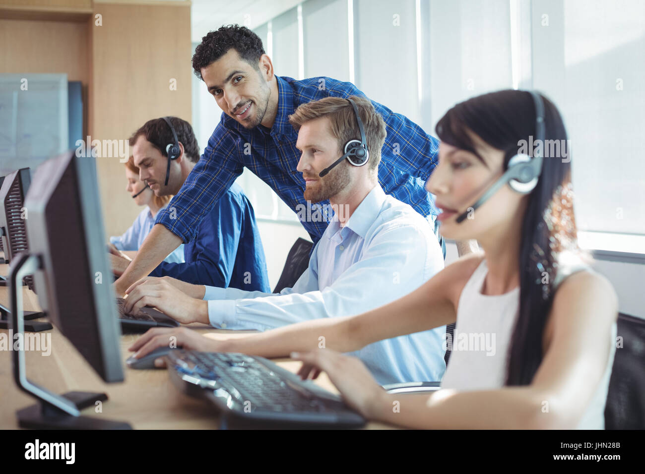 Lächelnd männlichen Vorgesetzten Unterstützung Telemarketer am Schalter im Call-center Stockfoto