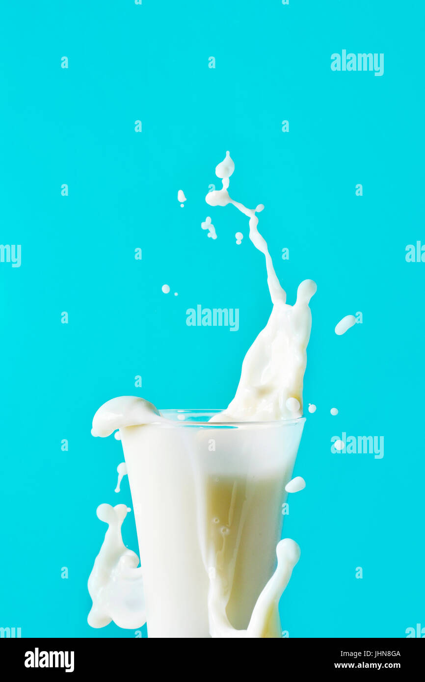 Nahaufnahme von einem Glas Milch spritzt überall auf blauem Hintergrund, mit einem negativen Raum an der Spitze Stockfoto