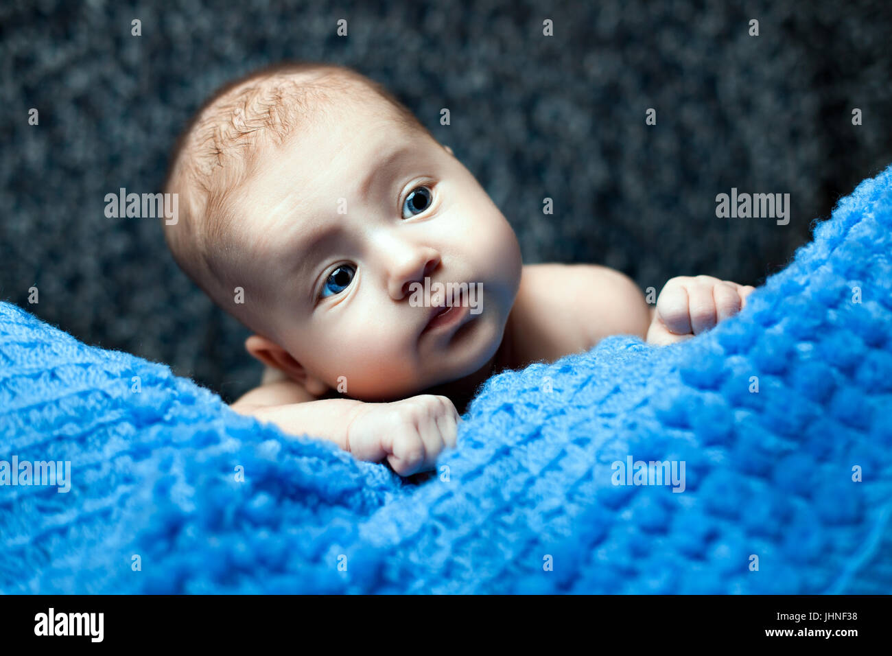 Baby Mädchen mit blauen Augen auf eine gestrickte Decke liegend und wegsehen Stockfoto