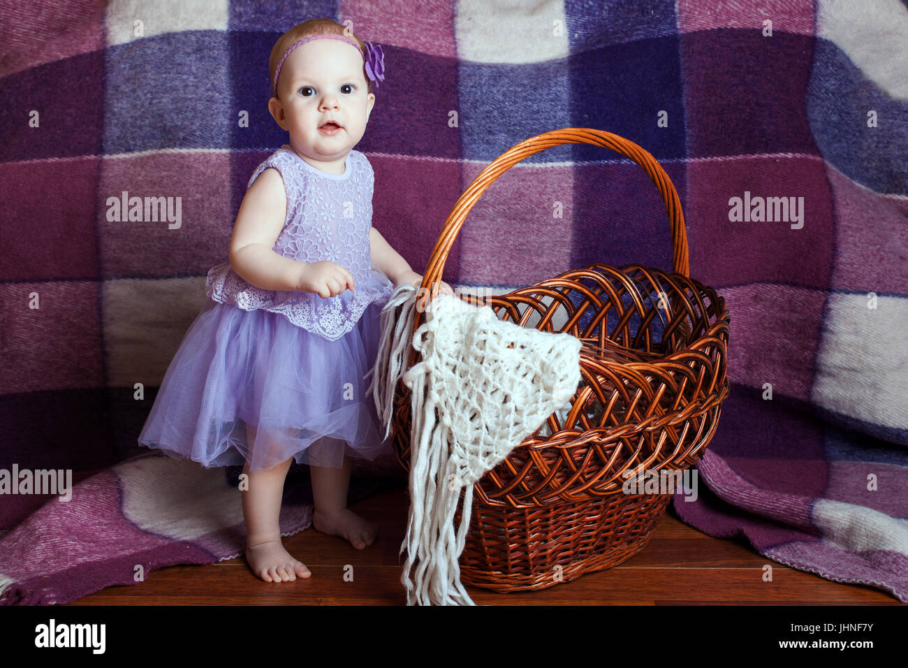Kleines Mädchen in einem wunderschönen Kleid steht in der Nähe einen Weidenkorb Stockfoto