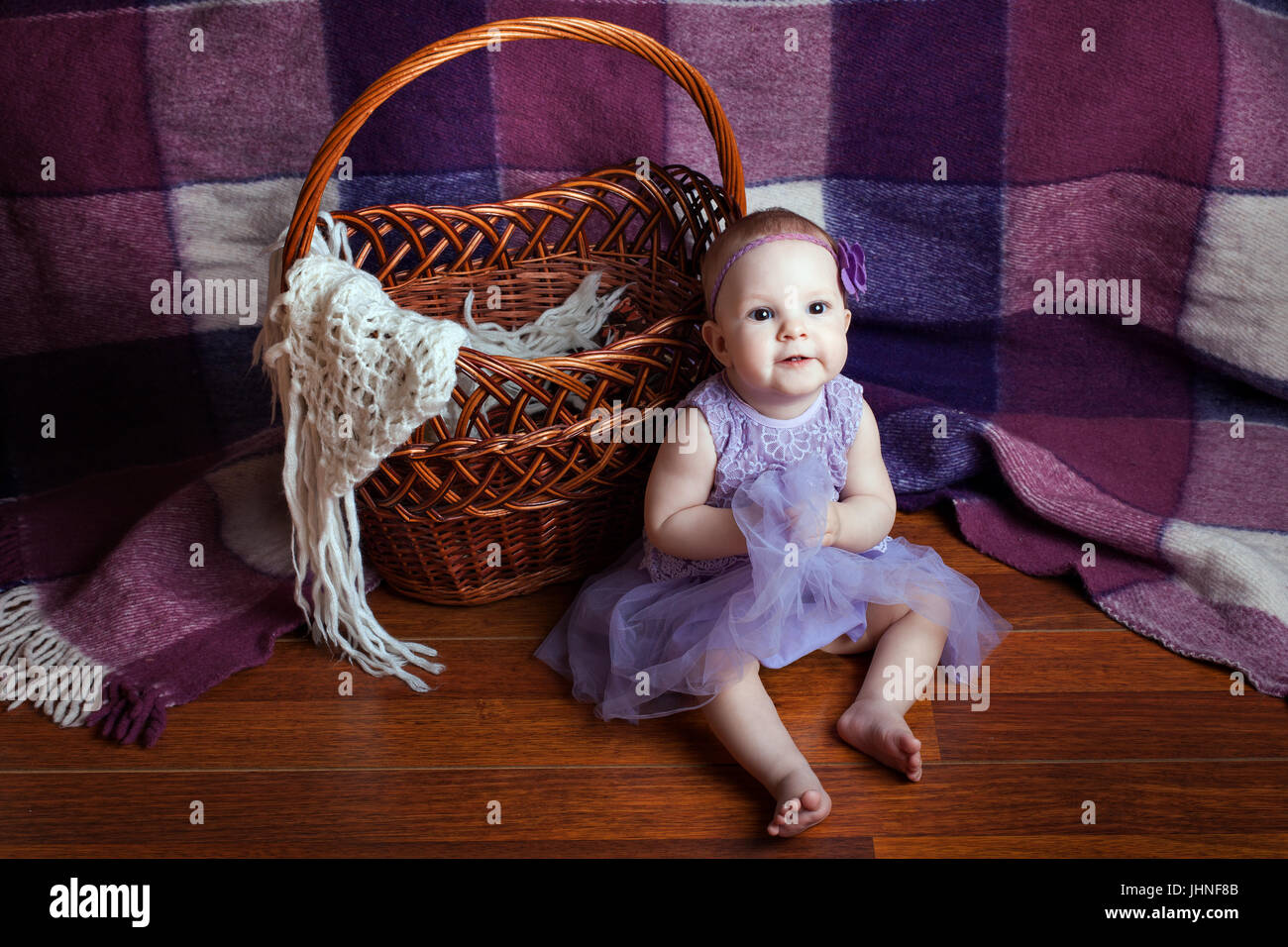 Kleines Mädchen in einem wunderschönen lila Kleid sitzt in der Nähe von Weidenkorb Stockfoto