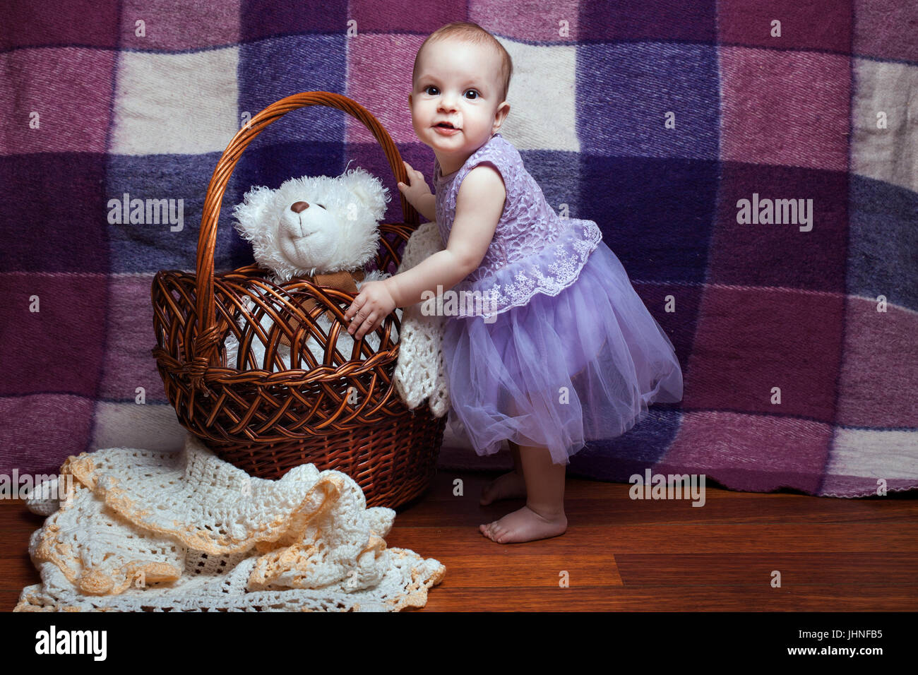 Niedliche kleine Mädchen in einem lila Kleid steht in der Nähe der Weidenkorb Stockfoto