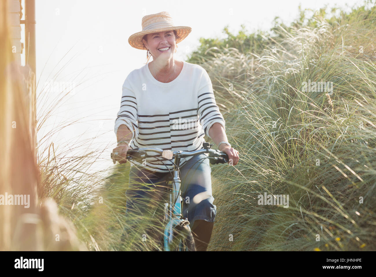 Reife Frau Reiten Fahrrad entlang Strandhafer lächelnd Stockfoto