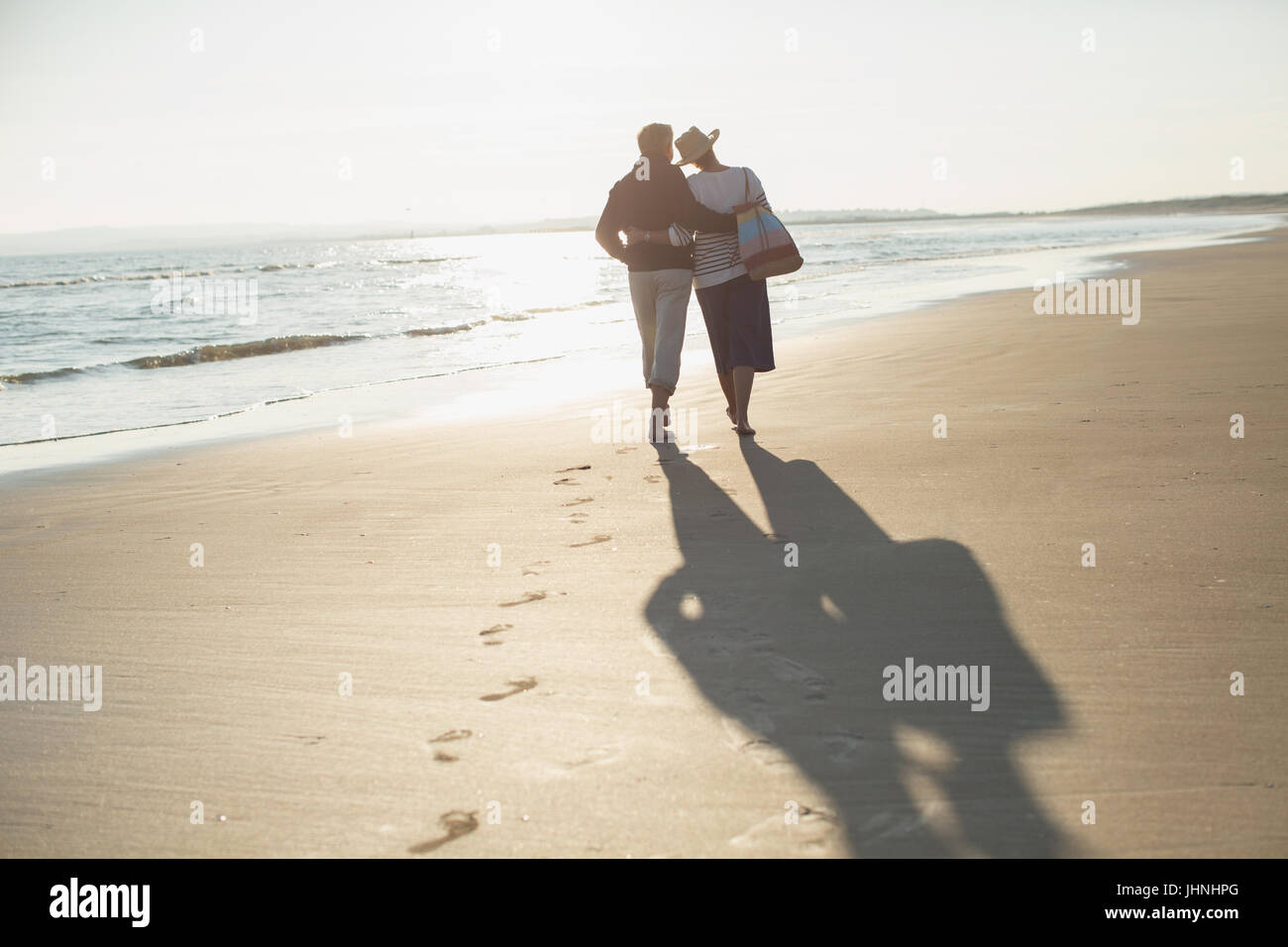 Älteres paar zärtlich umarmt und Wandern am sonnigen Strand Stockfoto