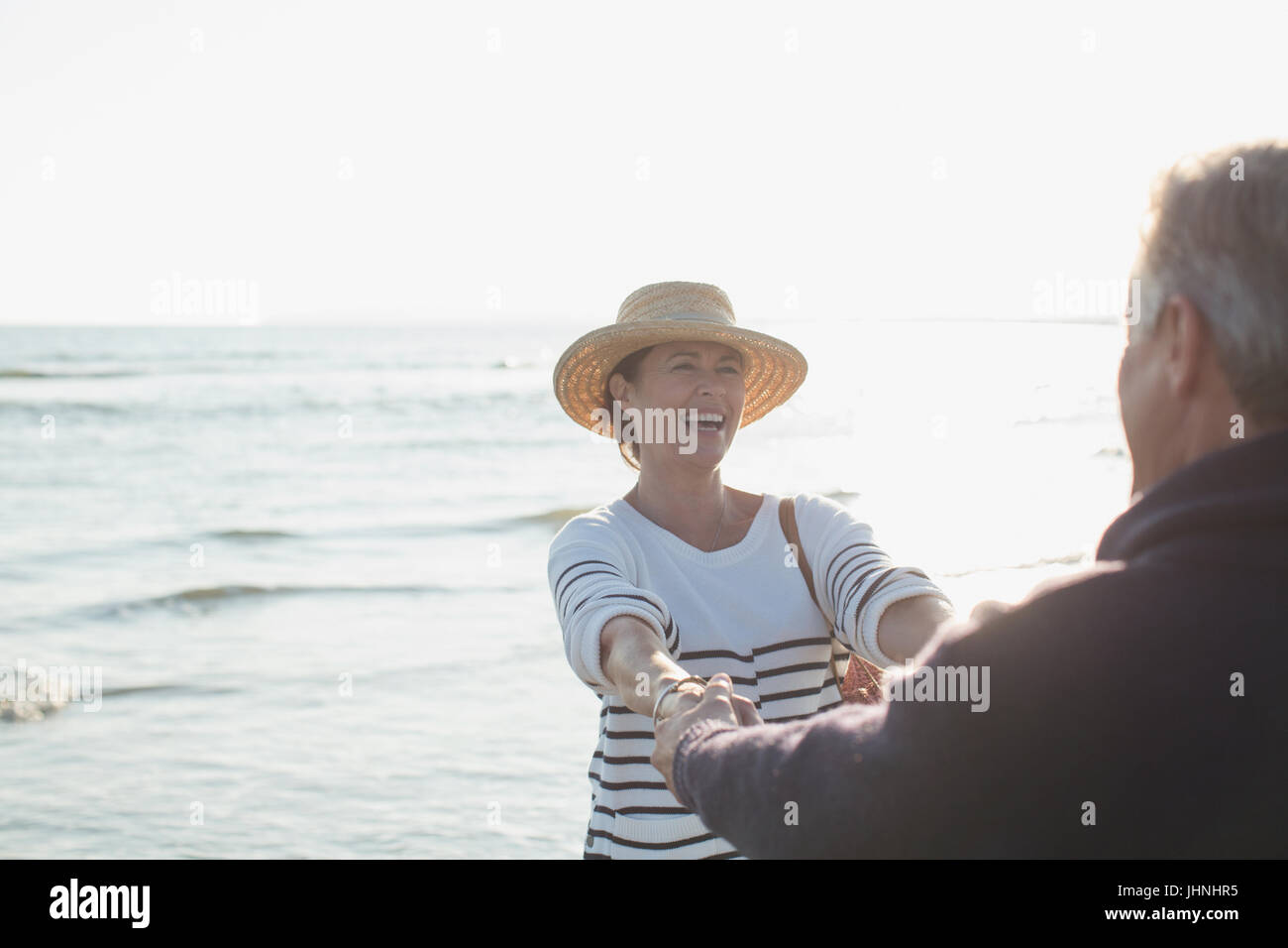 Spielerische älteres Paar halten die Hände am sonnigen Ocean beach Stockfoto