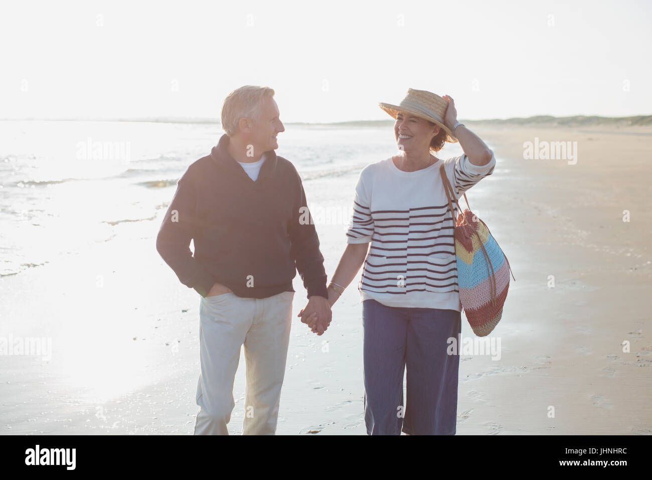 Älteres Paar Hand in Hand und Wandern am sonnigen Strand lächelnd Stockfoto